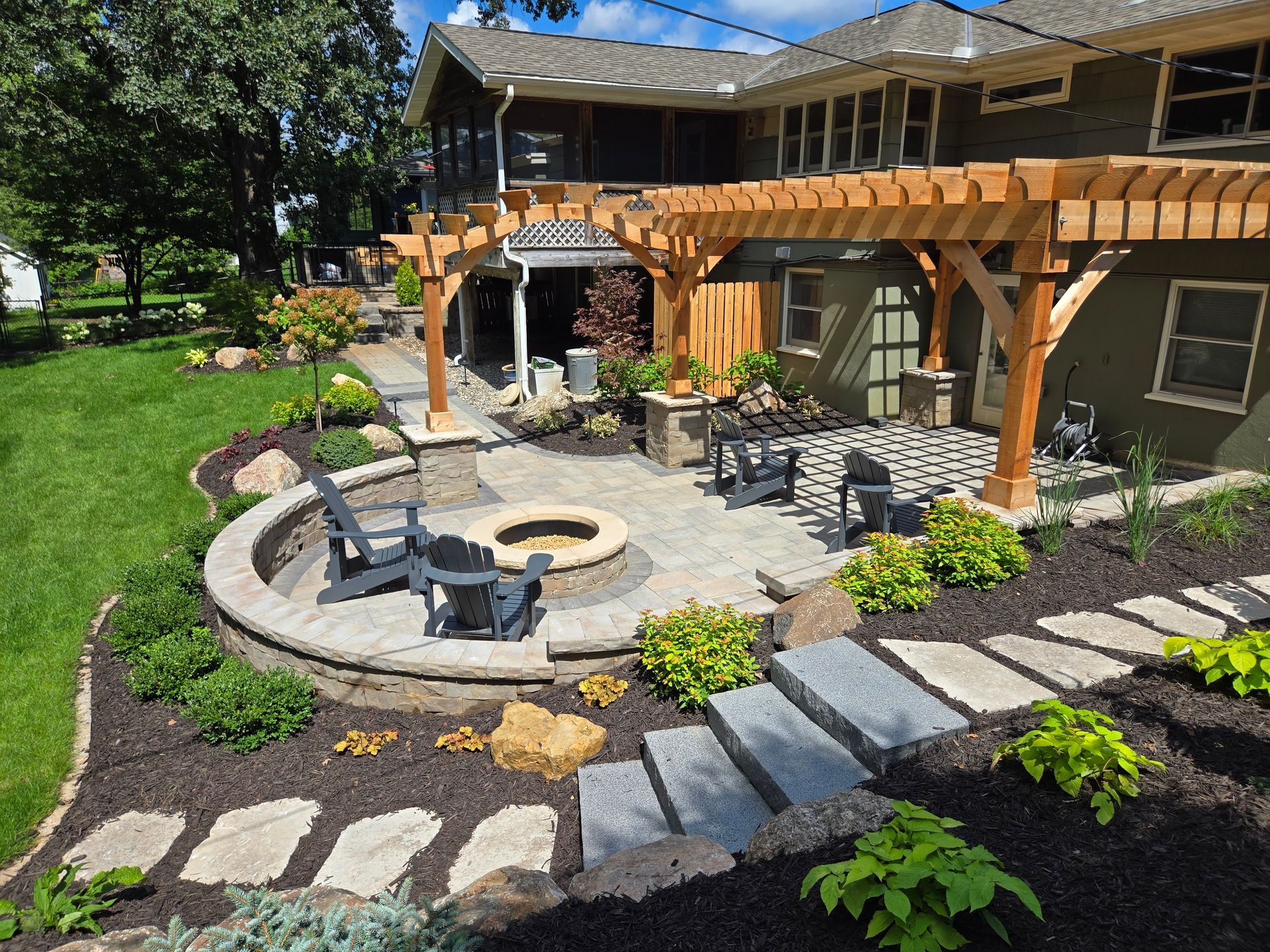 Backyard patio with fire pit, pergola, landscaping, and house.