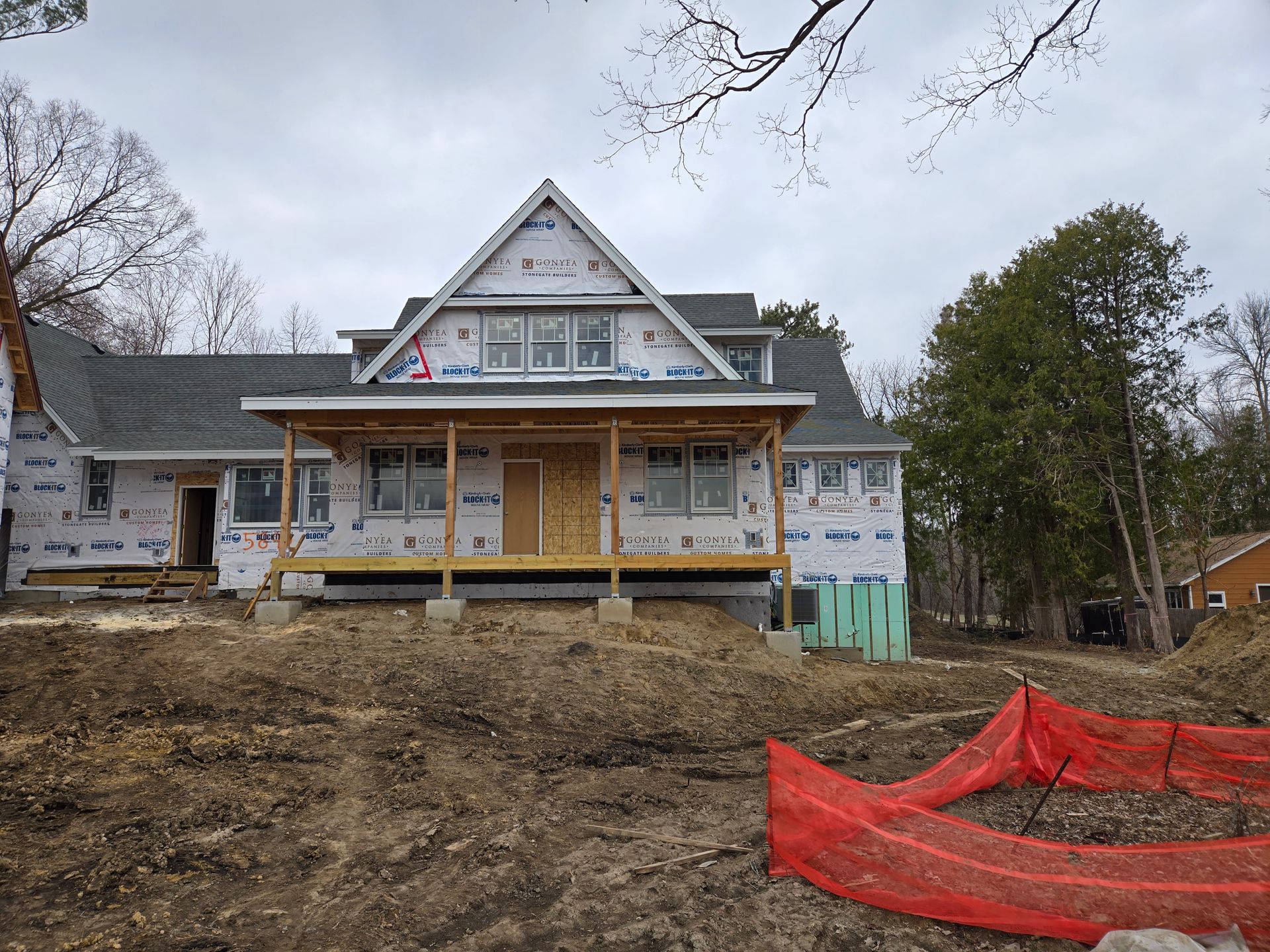 New house under construction with covered porch, blue tarp, and cloudy sky.