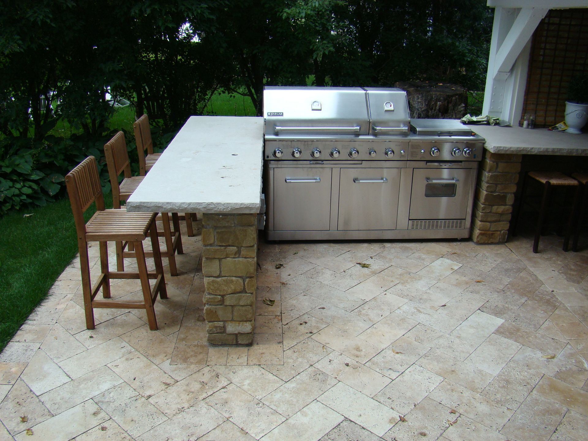 Outdoor kitchen with stainless steel grill, countertop seating, and stone patio.