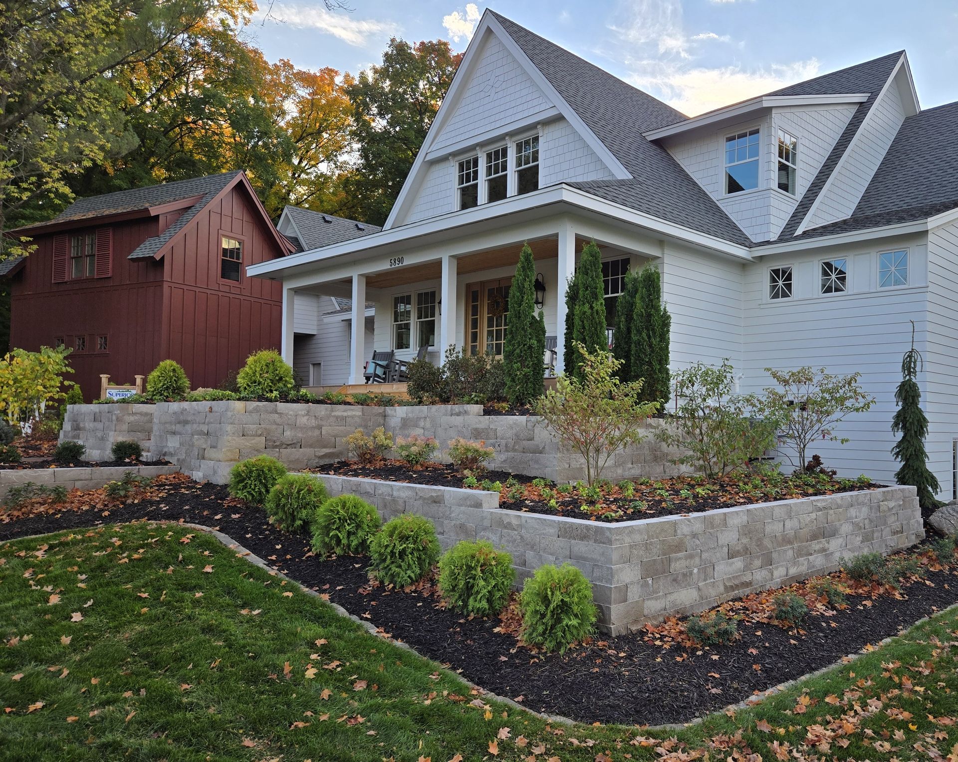 White house with tiered stone landscaping and a red barn in the background.
