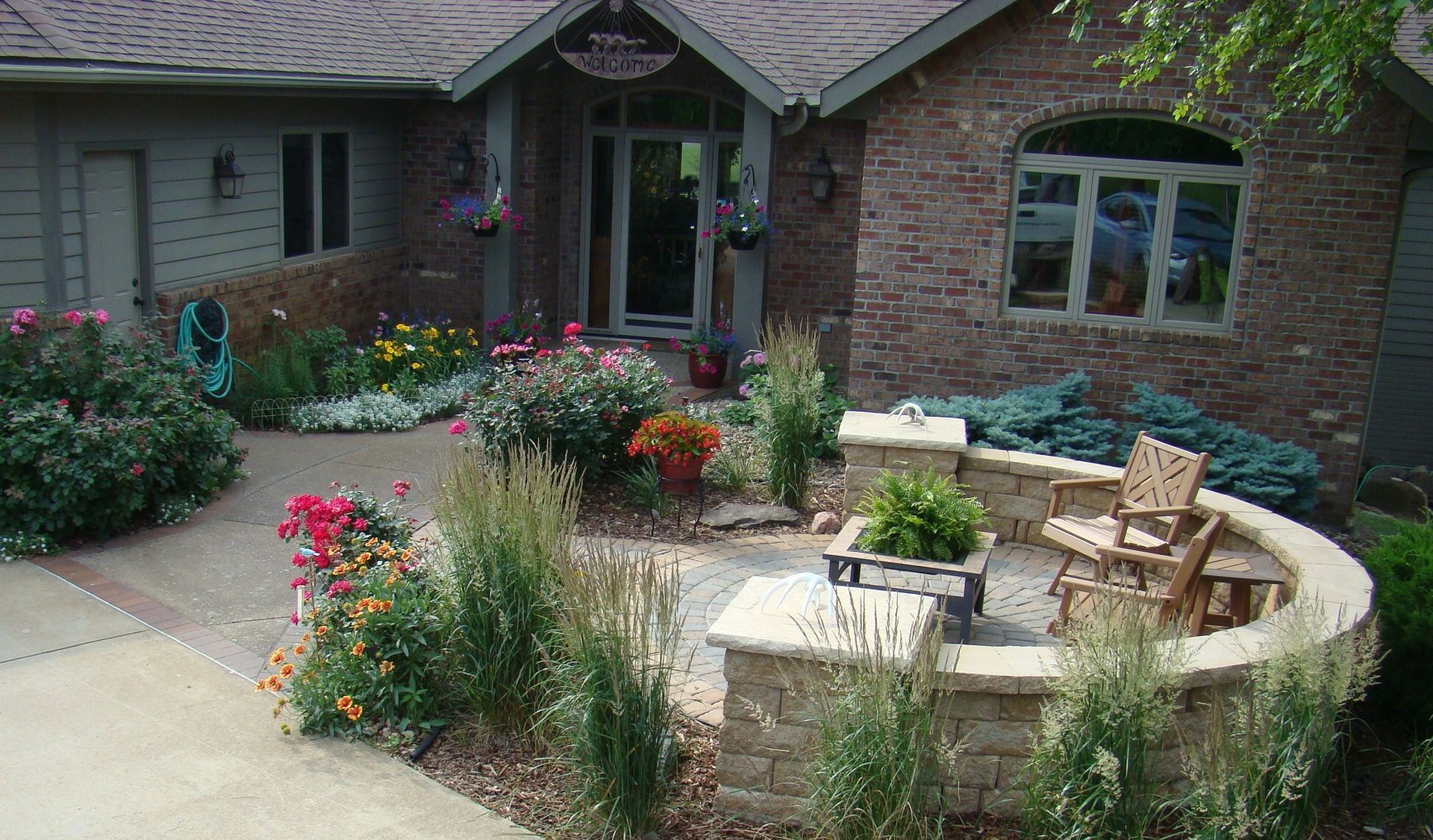 Brick house with landscaped yard and stone patio with chairs.