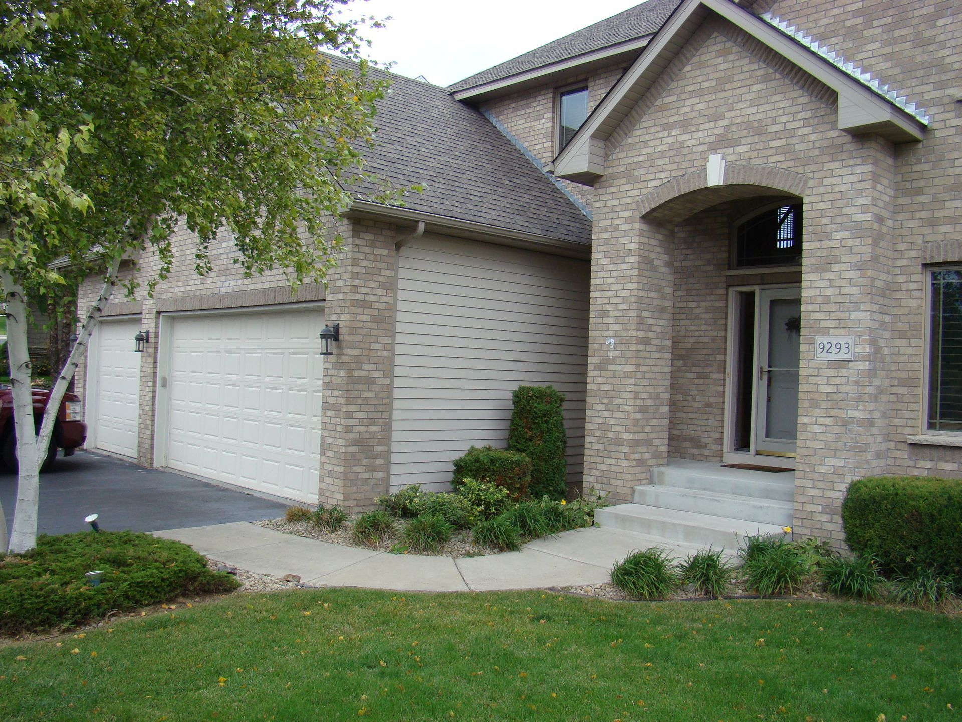 Exterior of a house with a garage, brick facade, arched entryway, and landscaping.