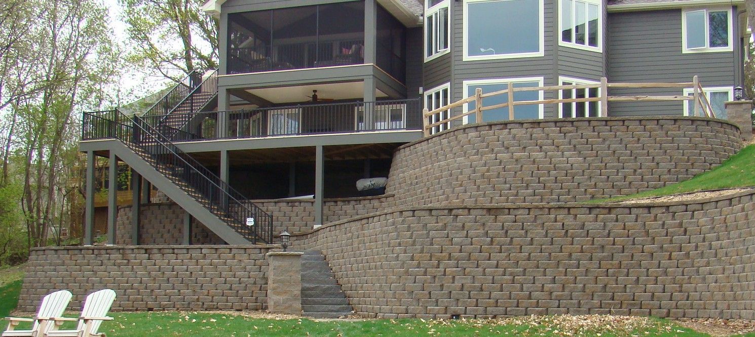 A multi-level home with a retaining wall, deck, and stairs built into a hillside.