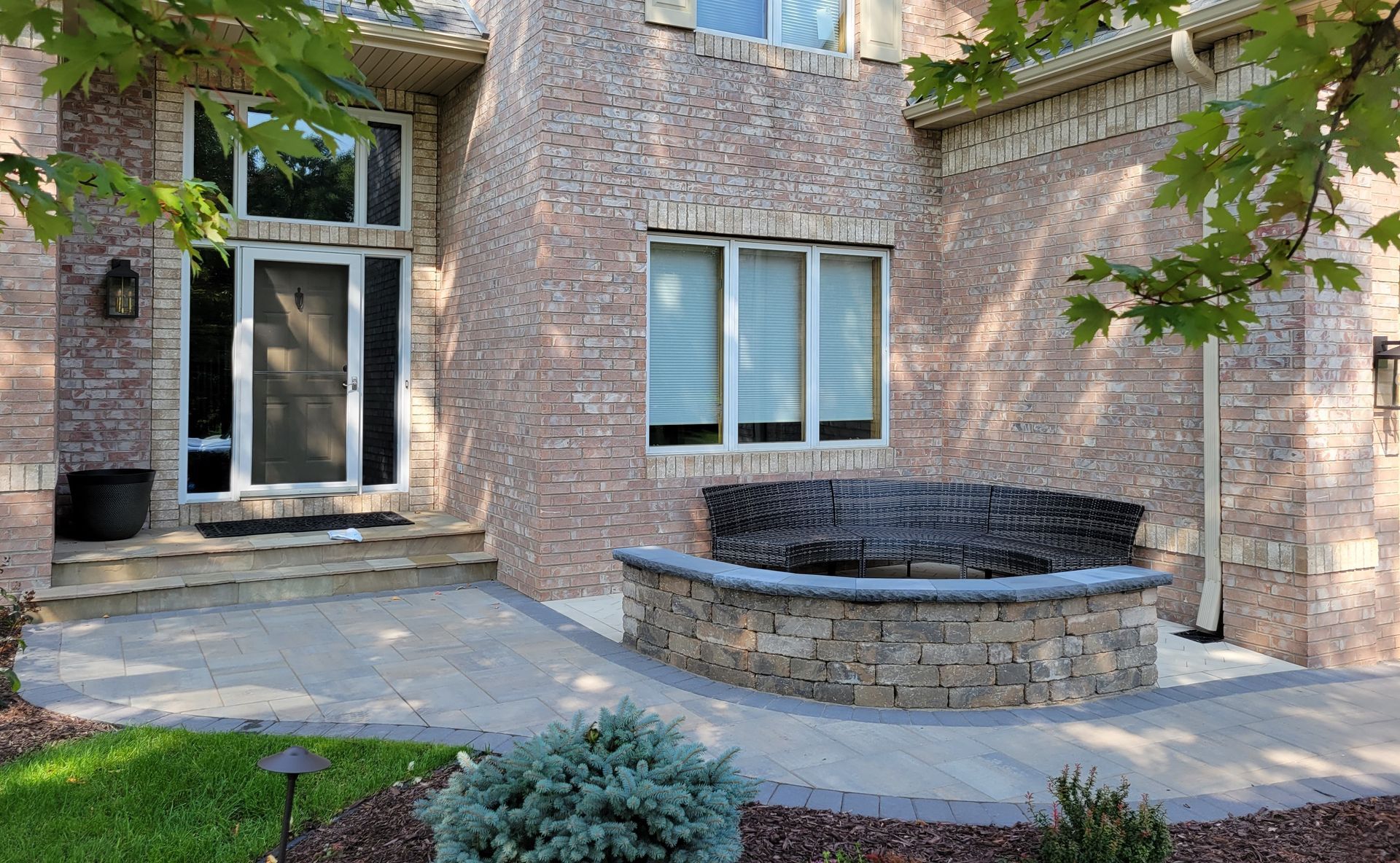 Brick house exterior with a stone-covered planter in front of a window, and a concrete pathway.
