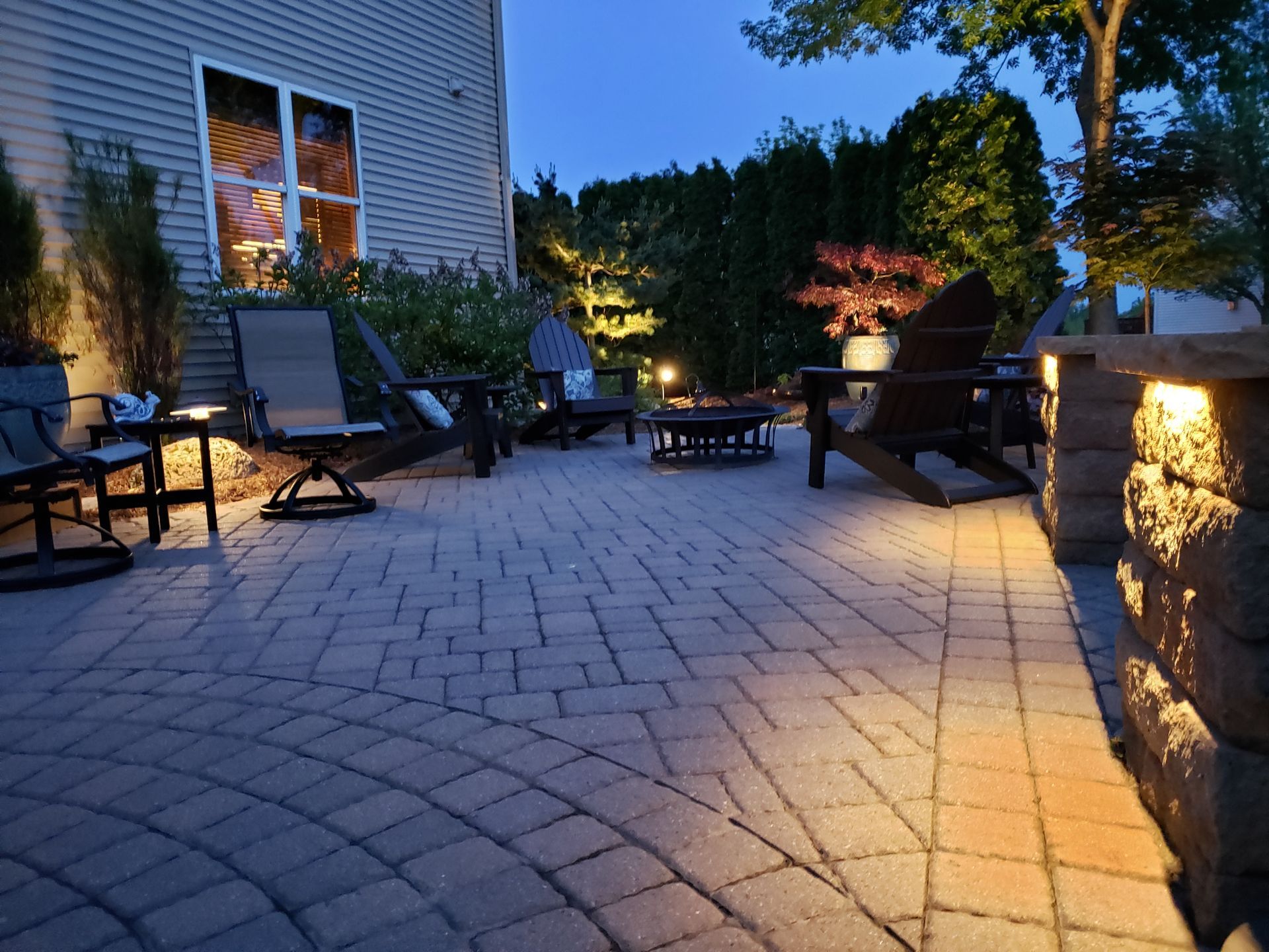 Brick patio at dusk with illuminated seating and landscaping.