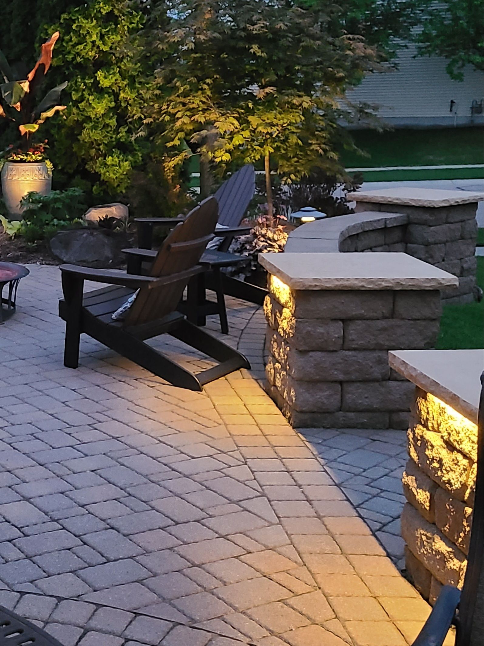 Patio with Adirondack chairs, low stone walls with lighting, and brick pavers. Evening setting.