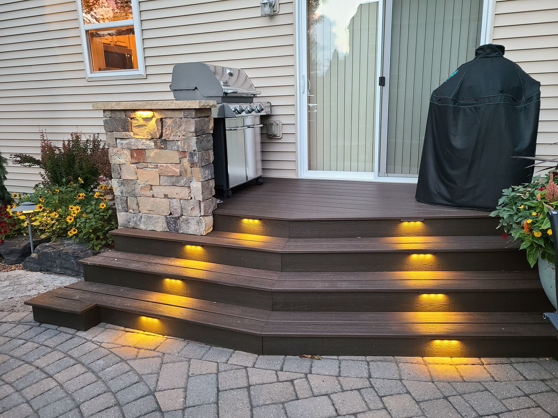 Composite deck steps with integrated lights leading to a grill area and sliding glass door.