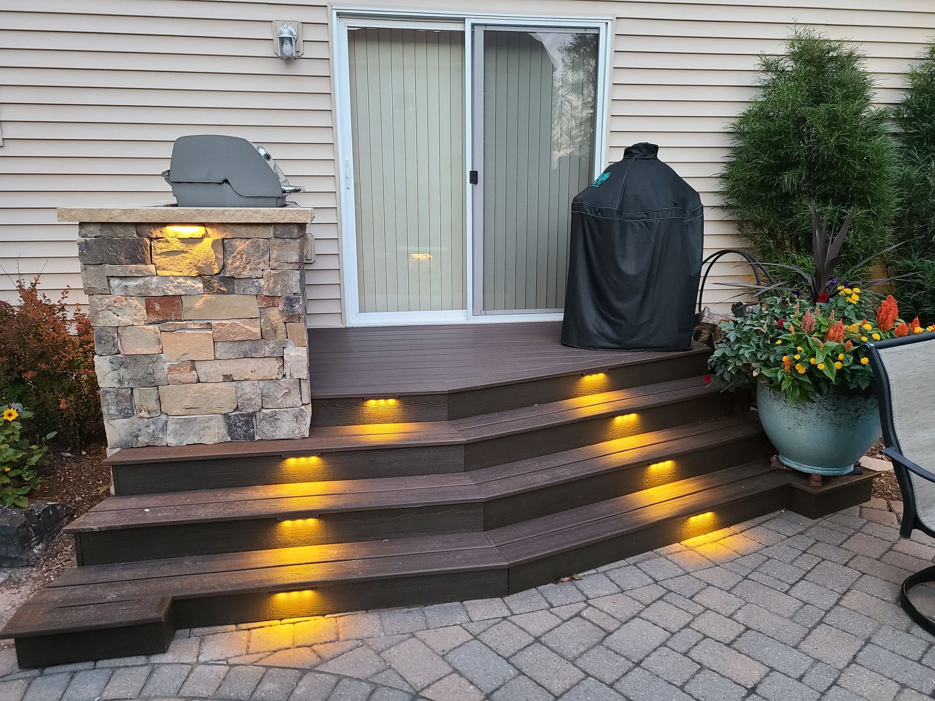 Outdoor steps with built-in lighting leading to a sliding glass door. A grill and a smoker are nearby.