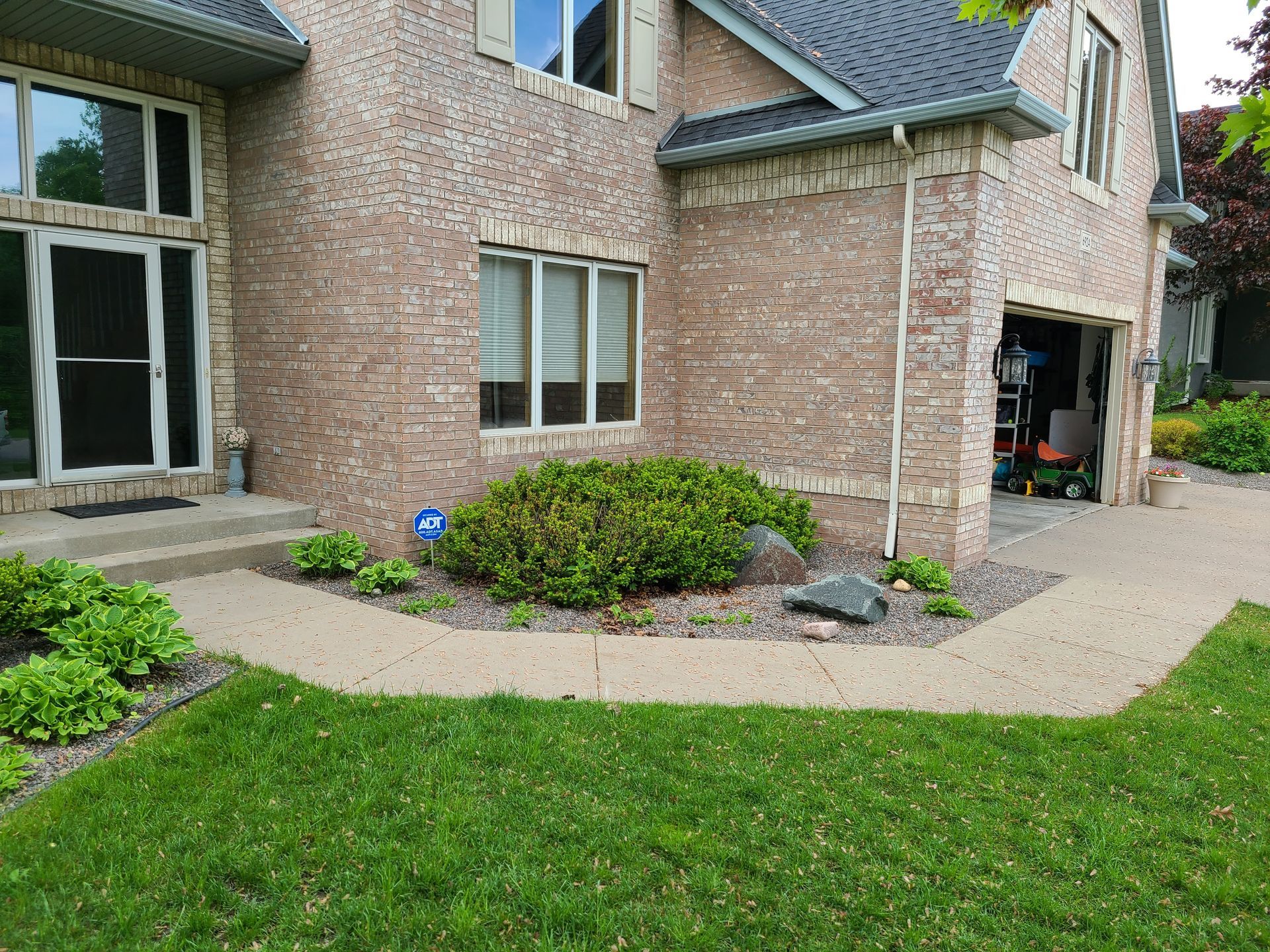Brick house exterior with a green lawn, sidewalk, and garden bed.