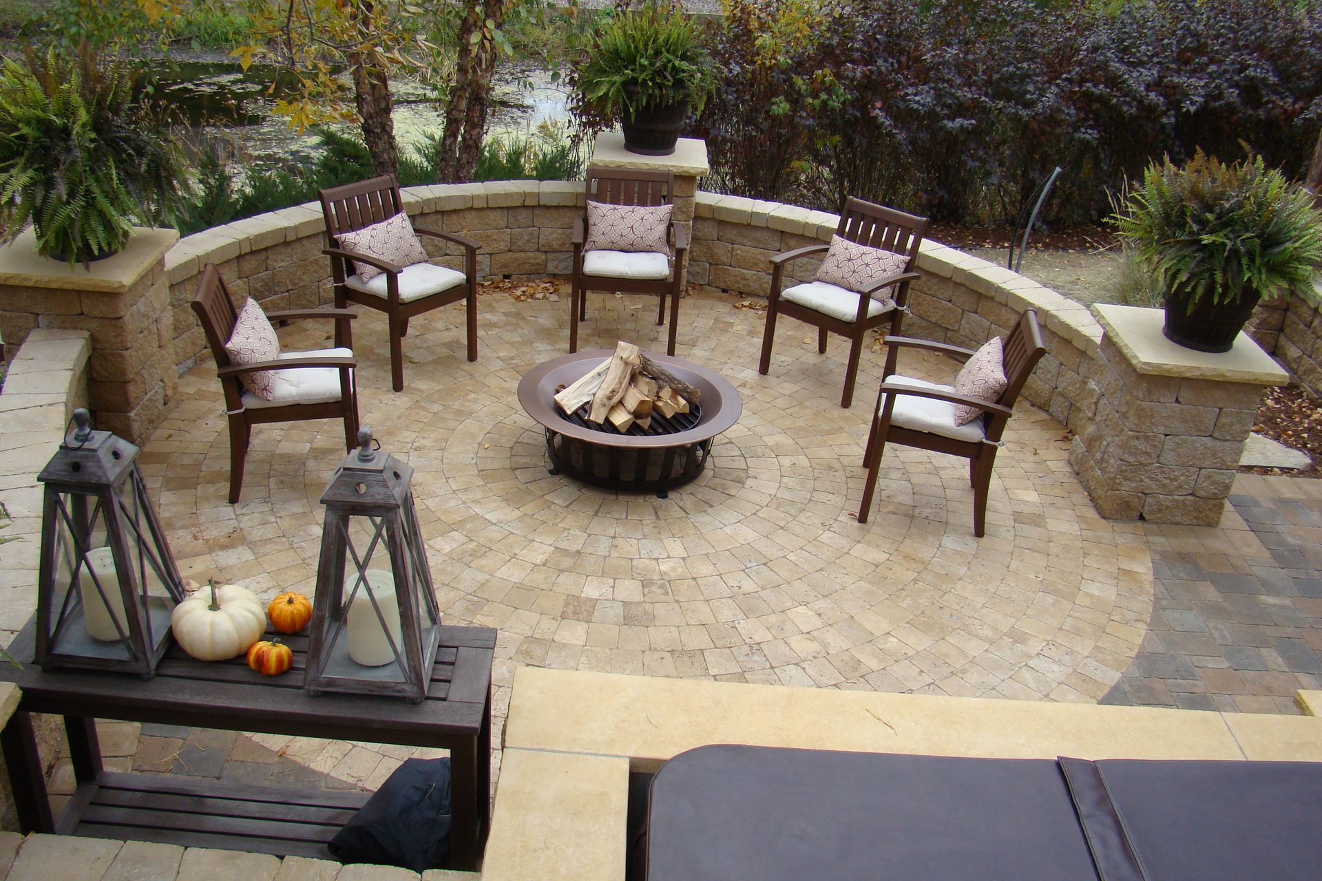 Outdoor patio with fire pit, seating, stone wall, and plants.