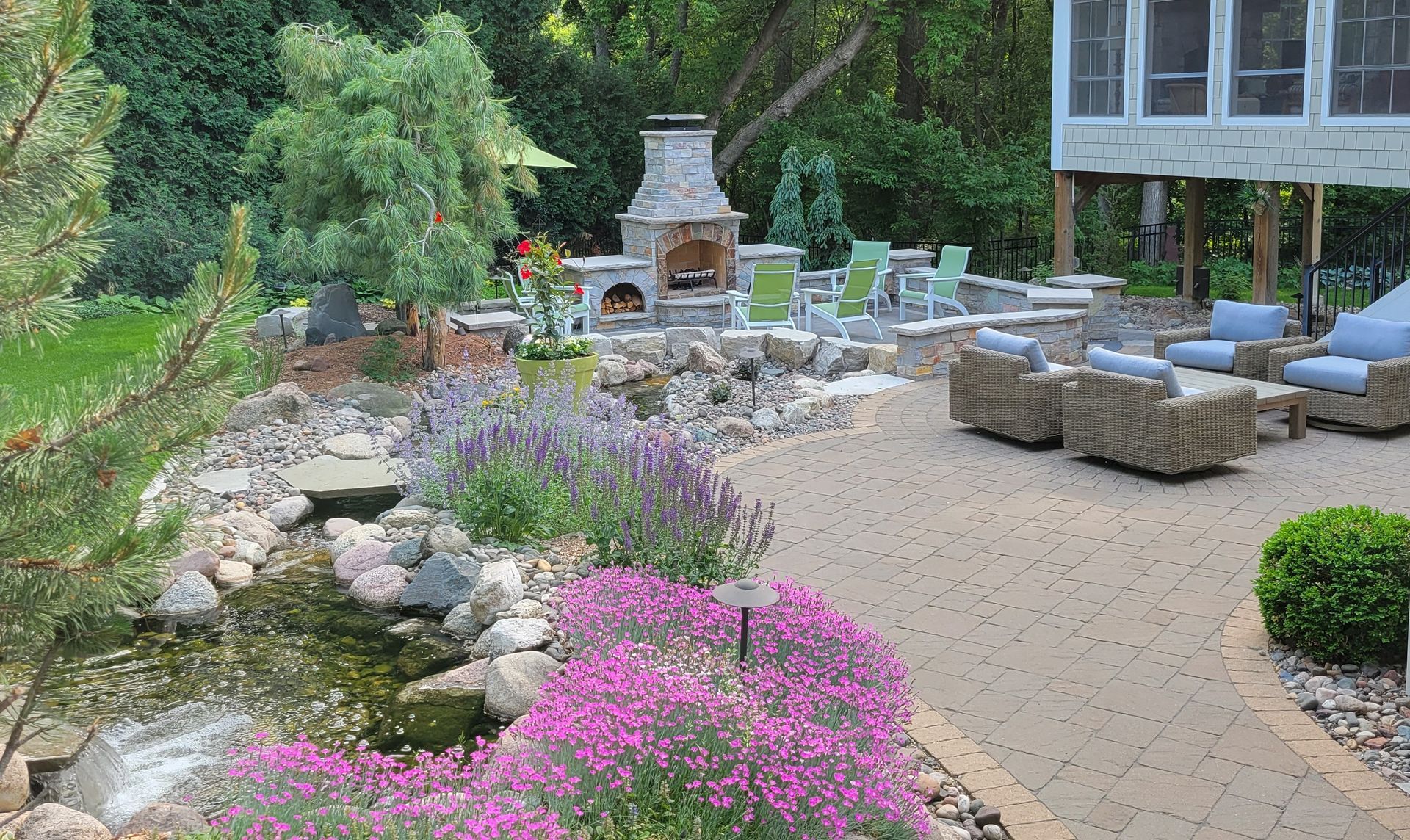 Stone patio with seating areas, a fireplace, water feature, and lush landscaping.
