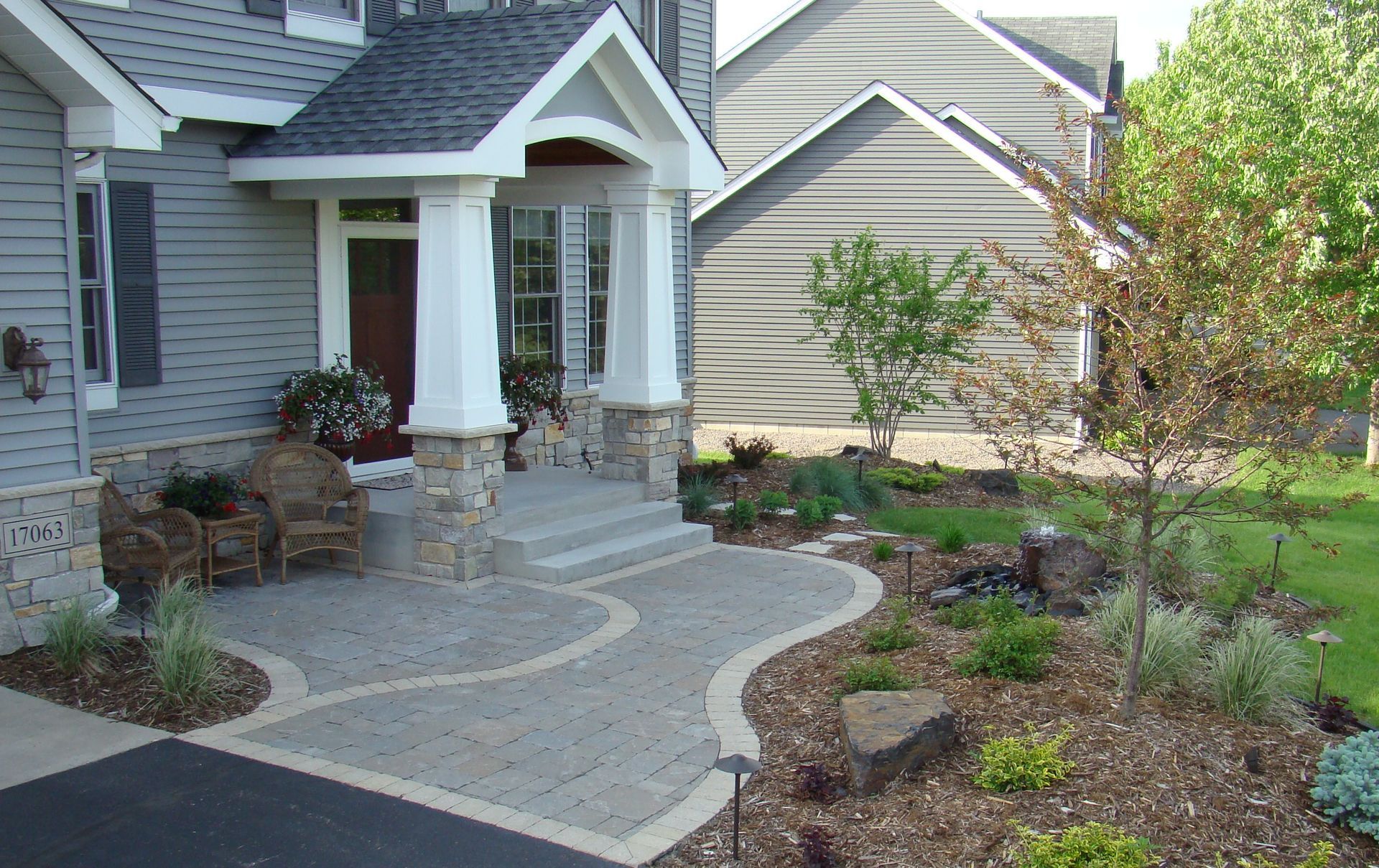 House exterior with a stone walkway leading to a covered porch and front door. Landscaping includes trees and shrubs.