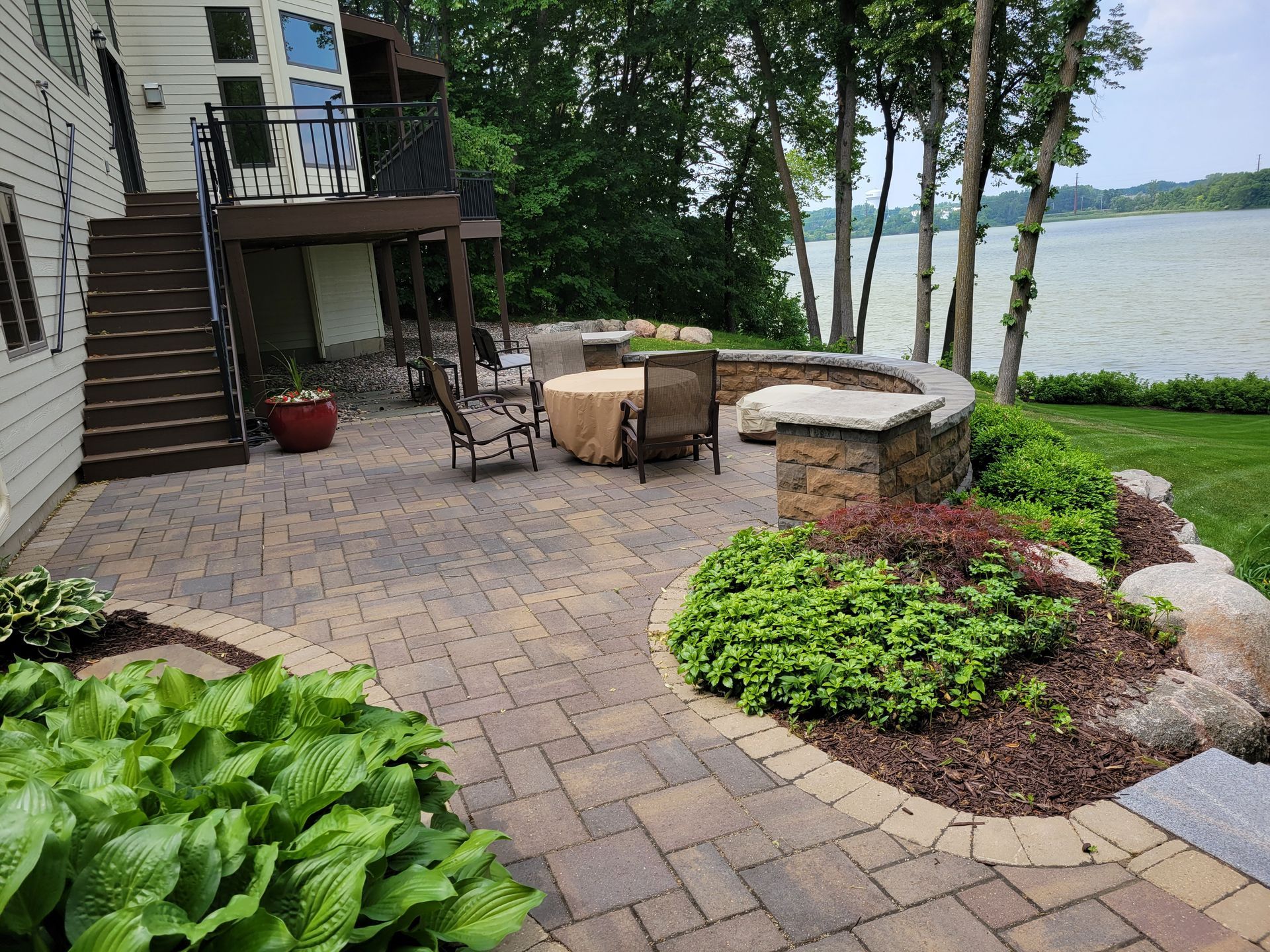 Patio with brick pavers, stone wall, table, chairs, and landscaping overlooking a lake.