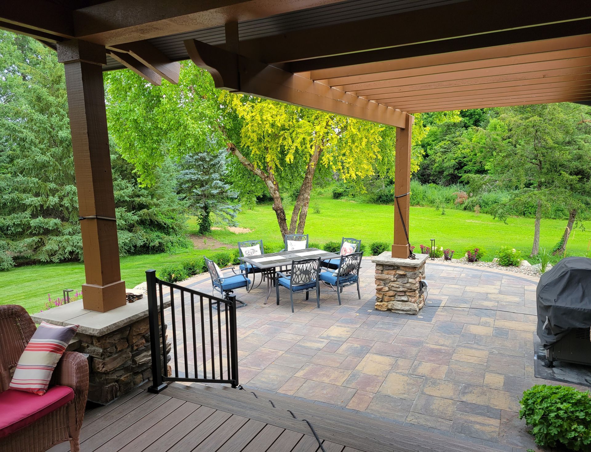 Patio with stone pavers, pergola, and outdoor dining set, overlooking a grassy backyard.