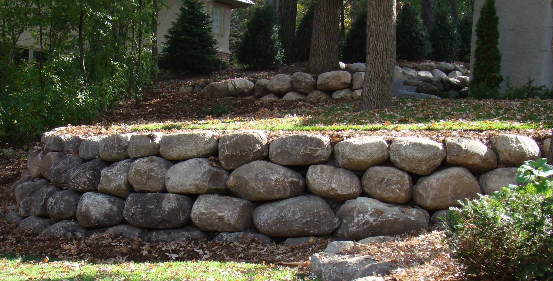 Stone retaining wall in a garden setting, holding back soil and supporting trees.