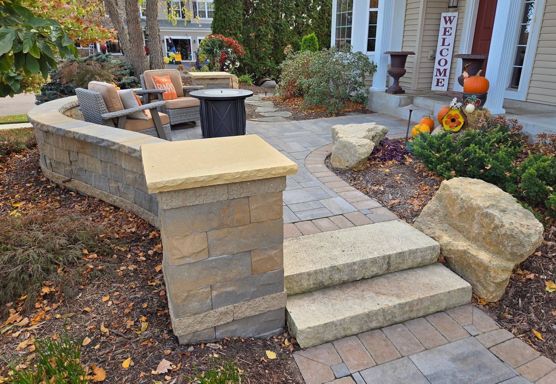 Stone patio with built-in seating area, steps, and pathway leading to a house with fall decorations.