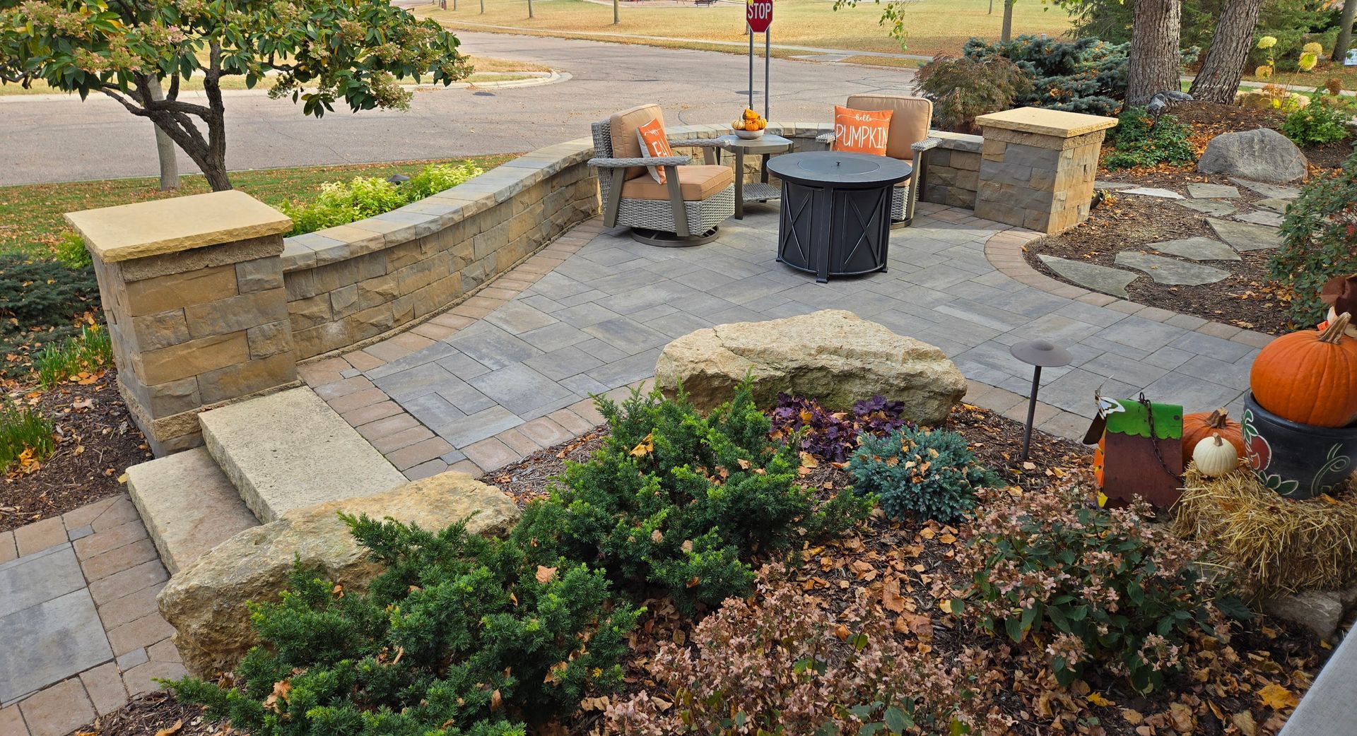 Stone patio with seating area, fire pit, and autumn decorations like pumpkins.