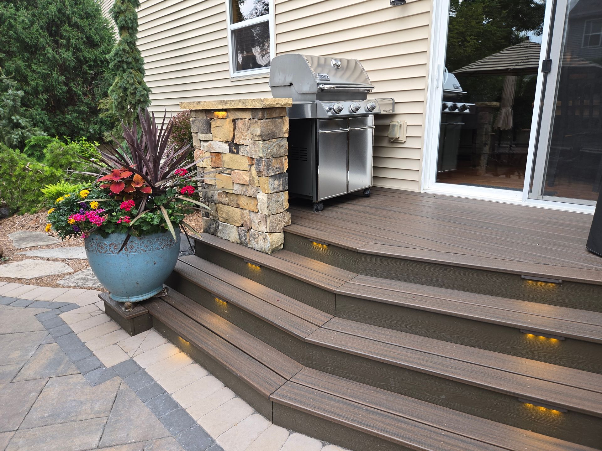 Outdoor deck with built-in grill and steps. A large potted plant sits beside the steps.