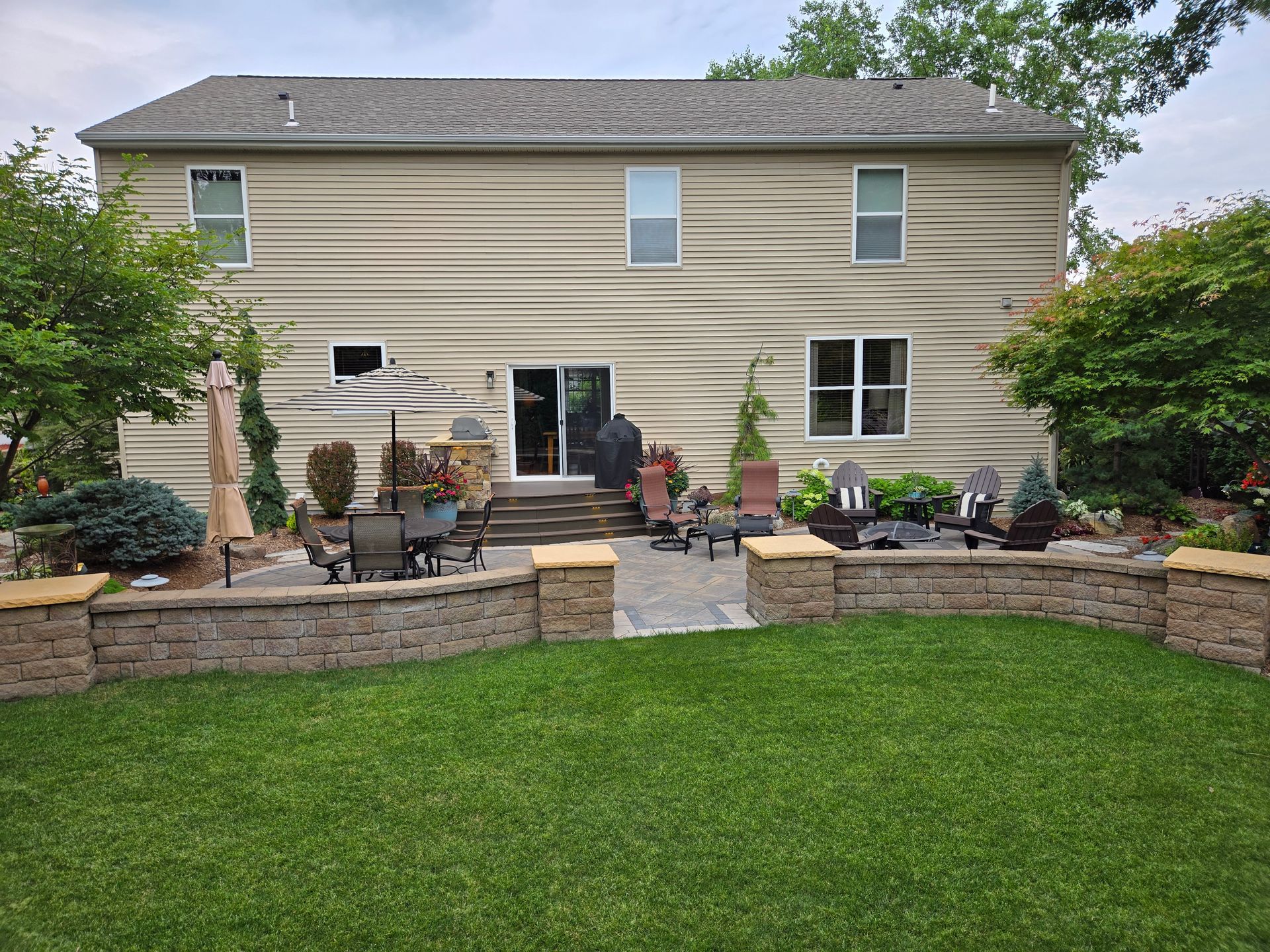 Backyard patio with lawn, retaining walls, seating, and a two-story house with wavy siding.
