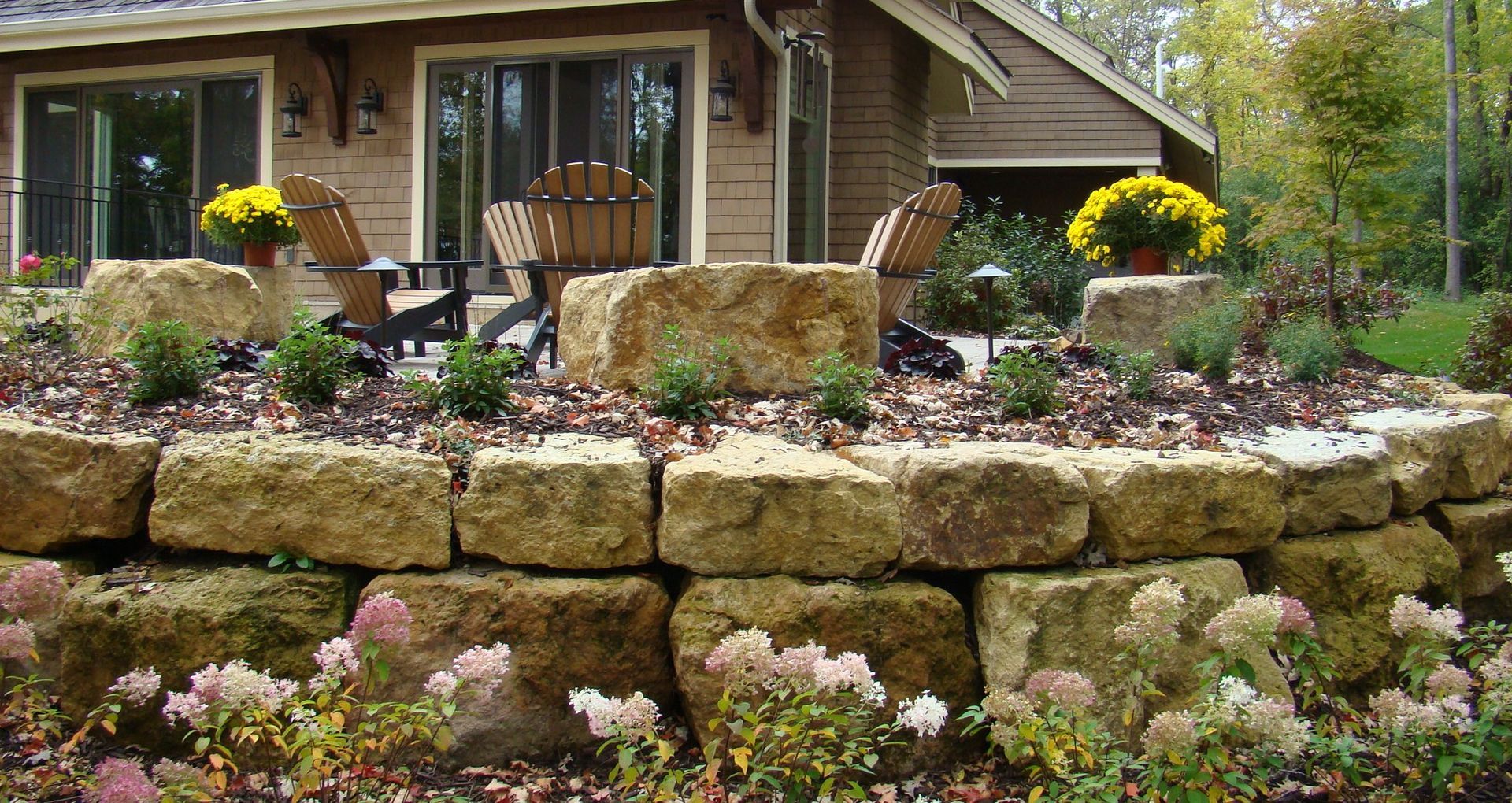 Stone retaining wall with flowers and seating area by a house.