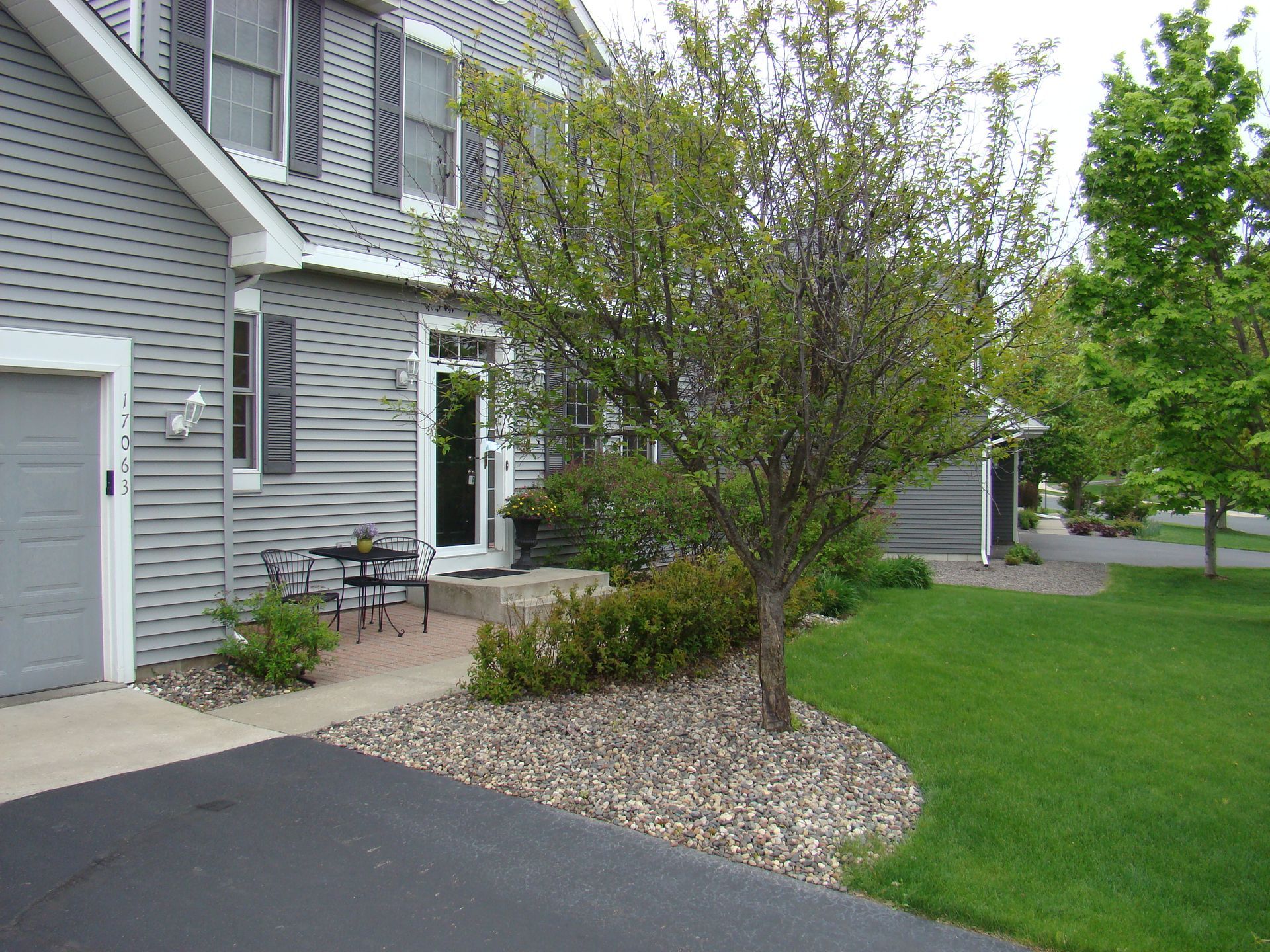 Gray house with shutters, small tree, patio furniture, and green lawn.