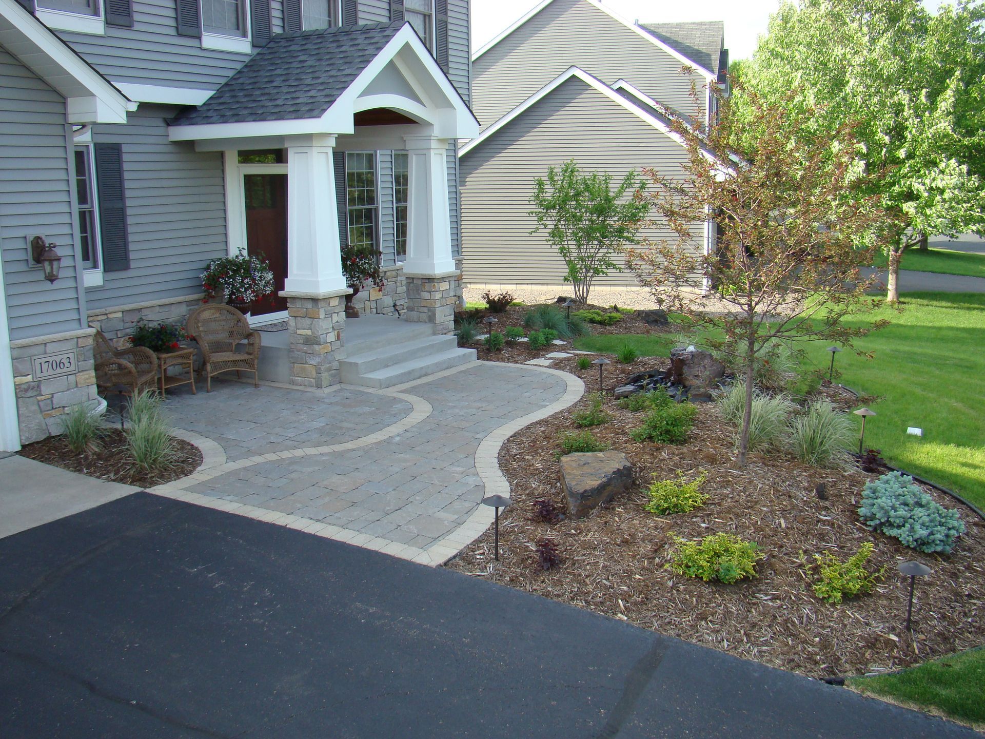 Gray house with stone columns, curved walkway, and landscaped yard.