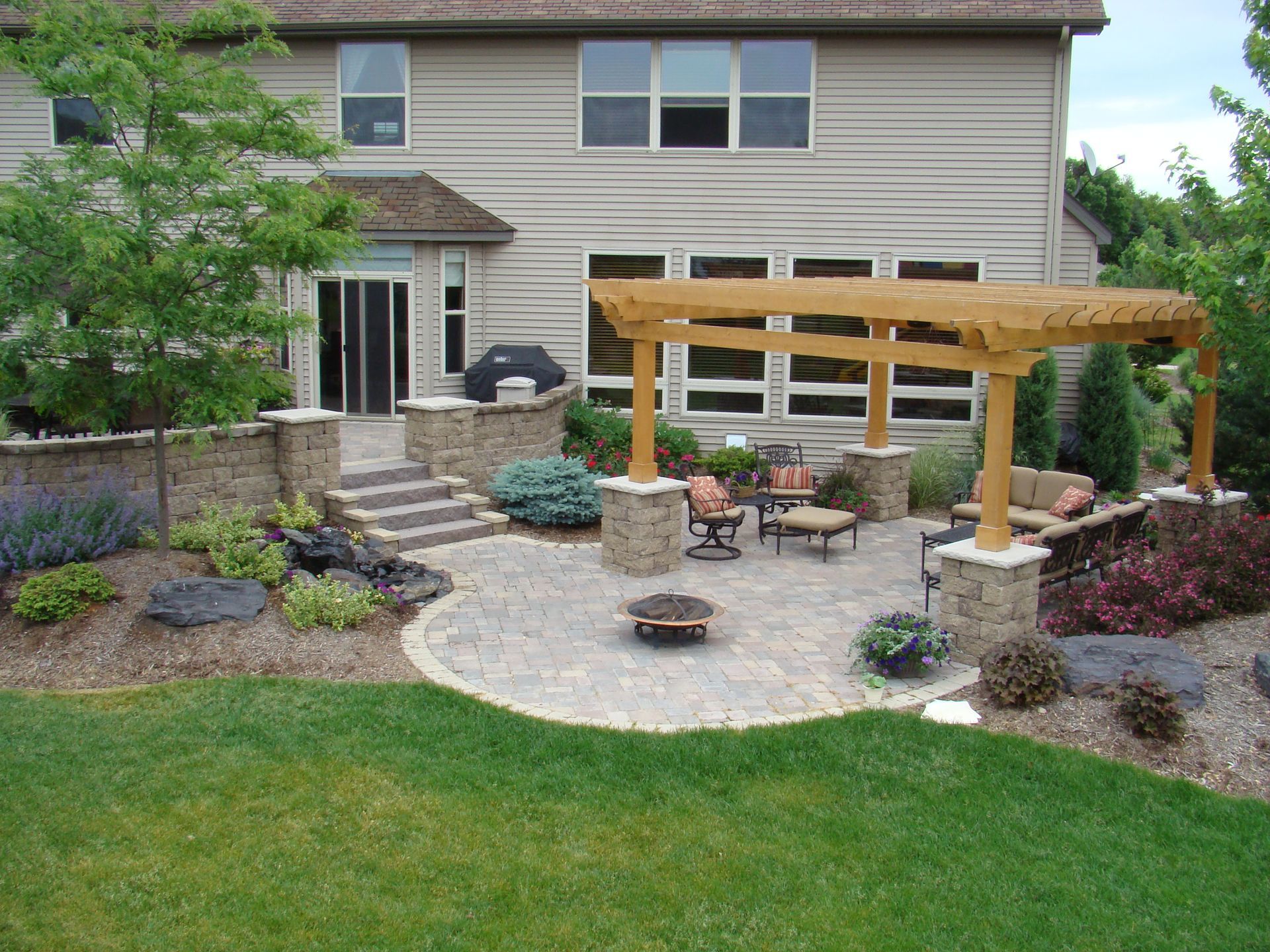 Backyard patio with pergola, seating, fire pit, stone walls, and landscaping.