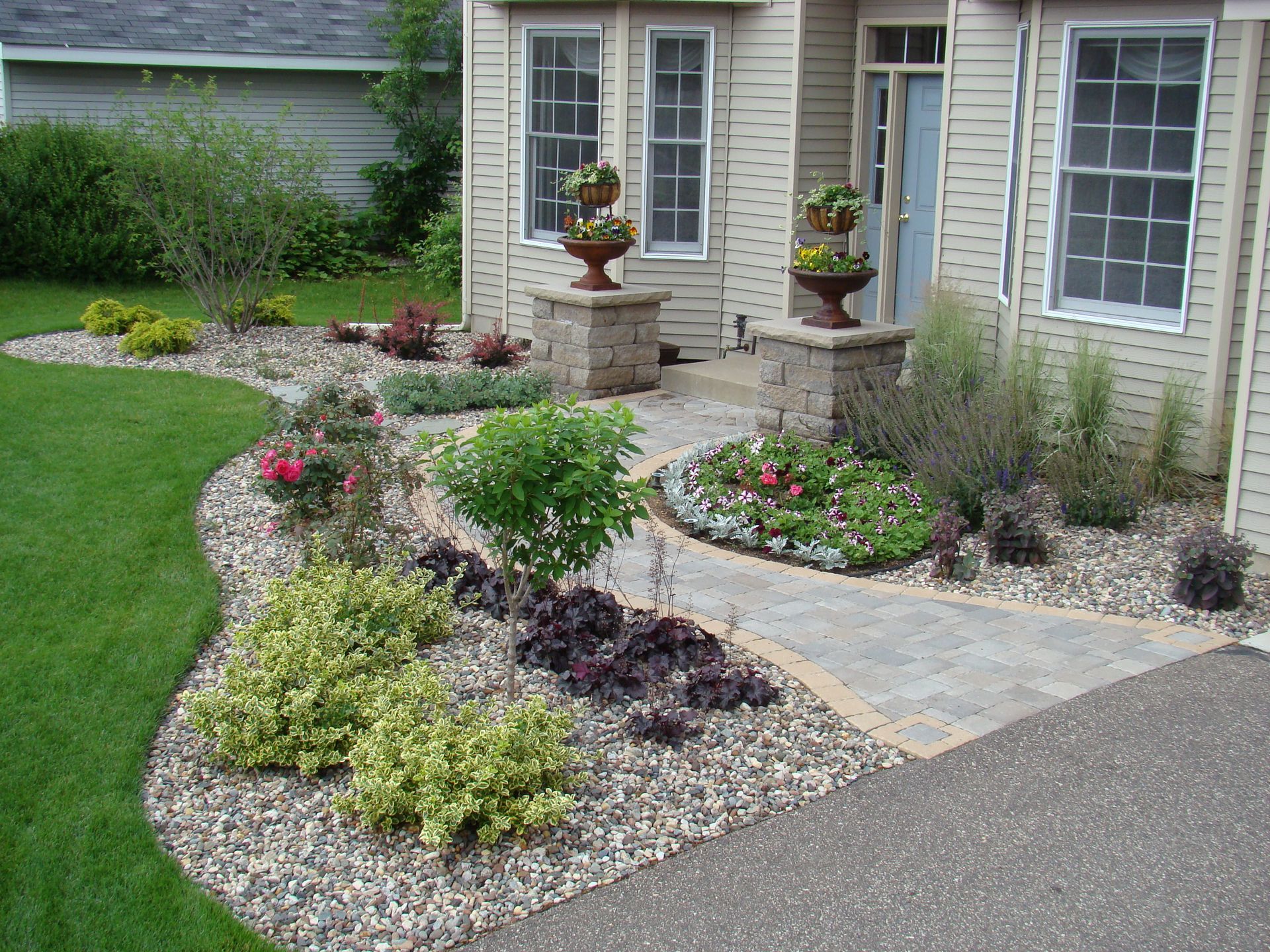 Landscaped yard with stone pathway and colorful flower beds leading to a house entrance.