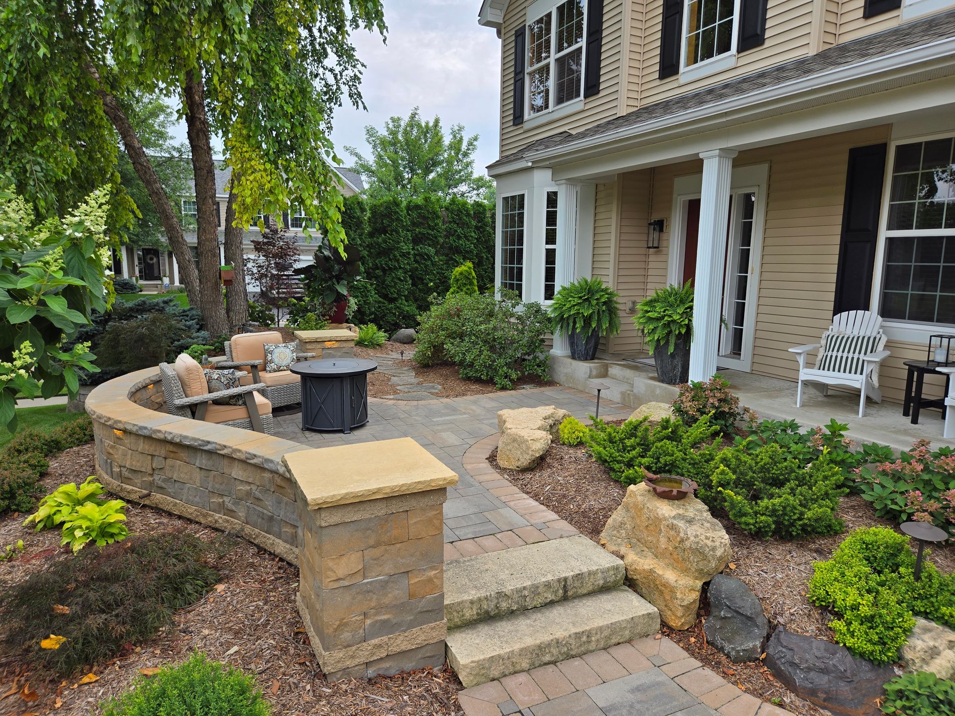 Stone patio with seating area, landscaped walkway, and beige house with porch.