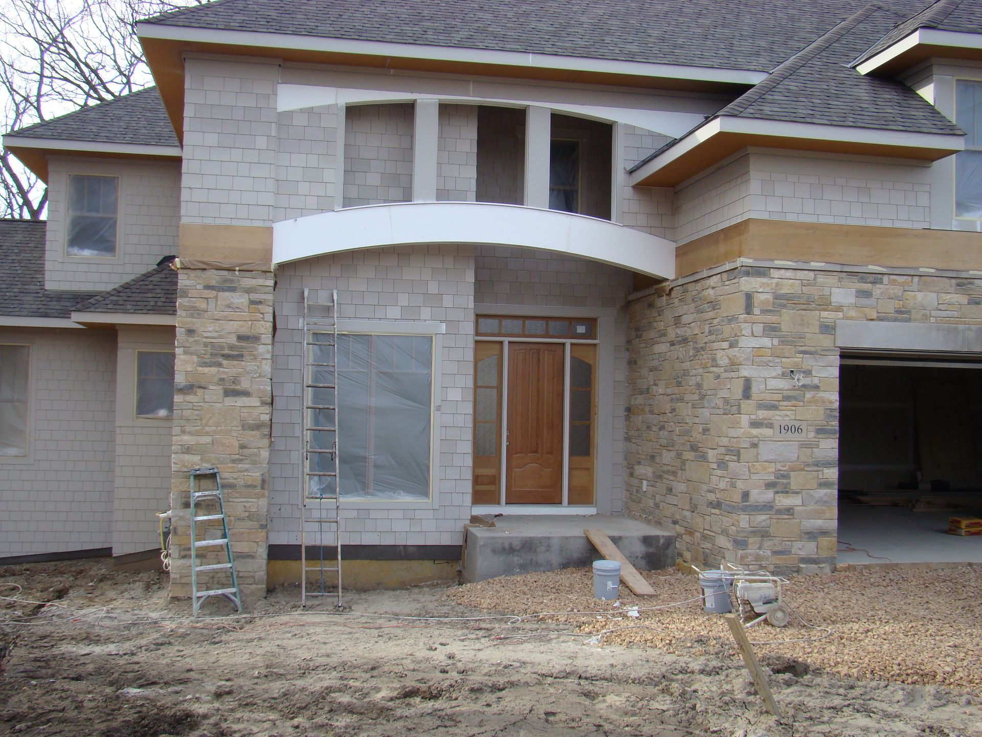 Stone-clad house under construction with arched entry, wooden door, and ladder outside.