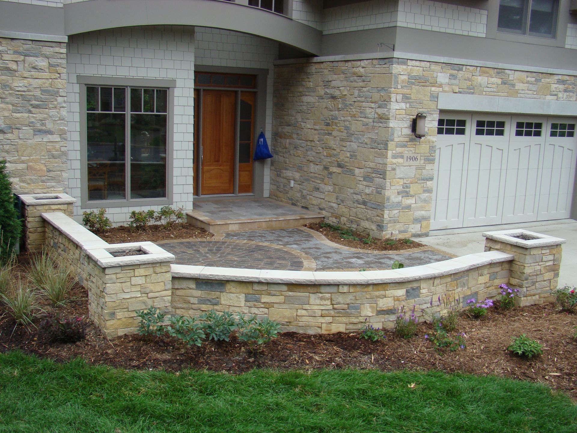 Stone facade of a home with a curved wall, door, and garage. Green grass and landscaping are in the foreground.