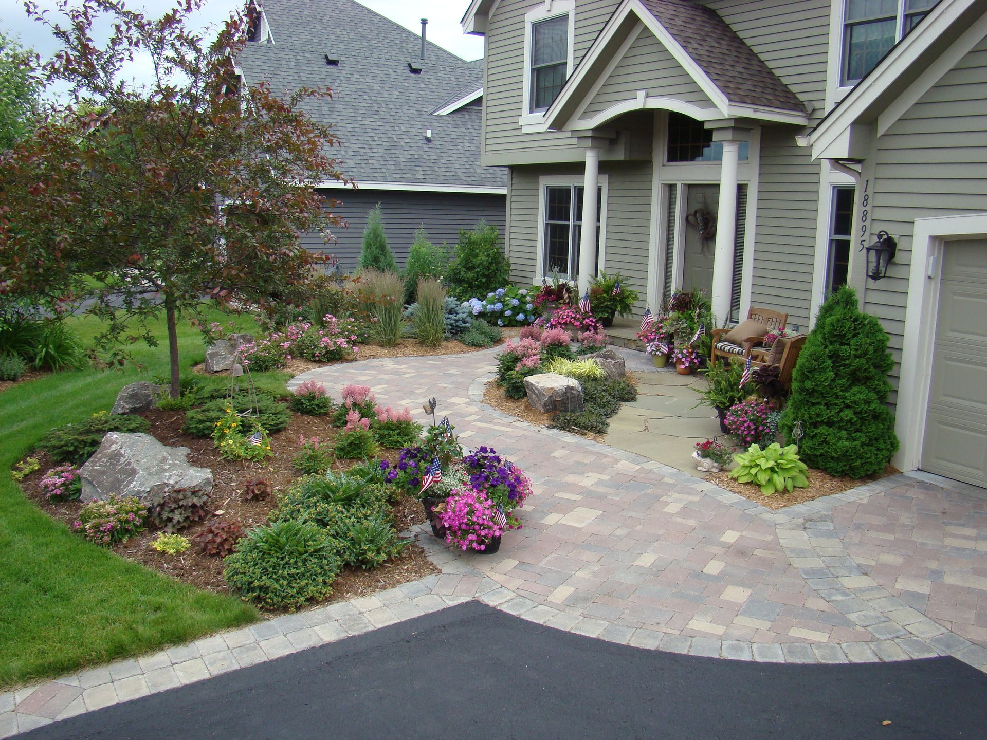 Well-landscaped home exterior with stone pathway, colorful flowers, and a tree.