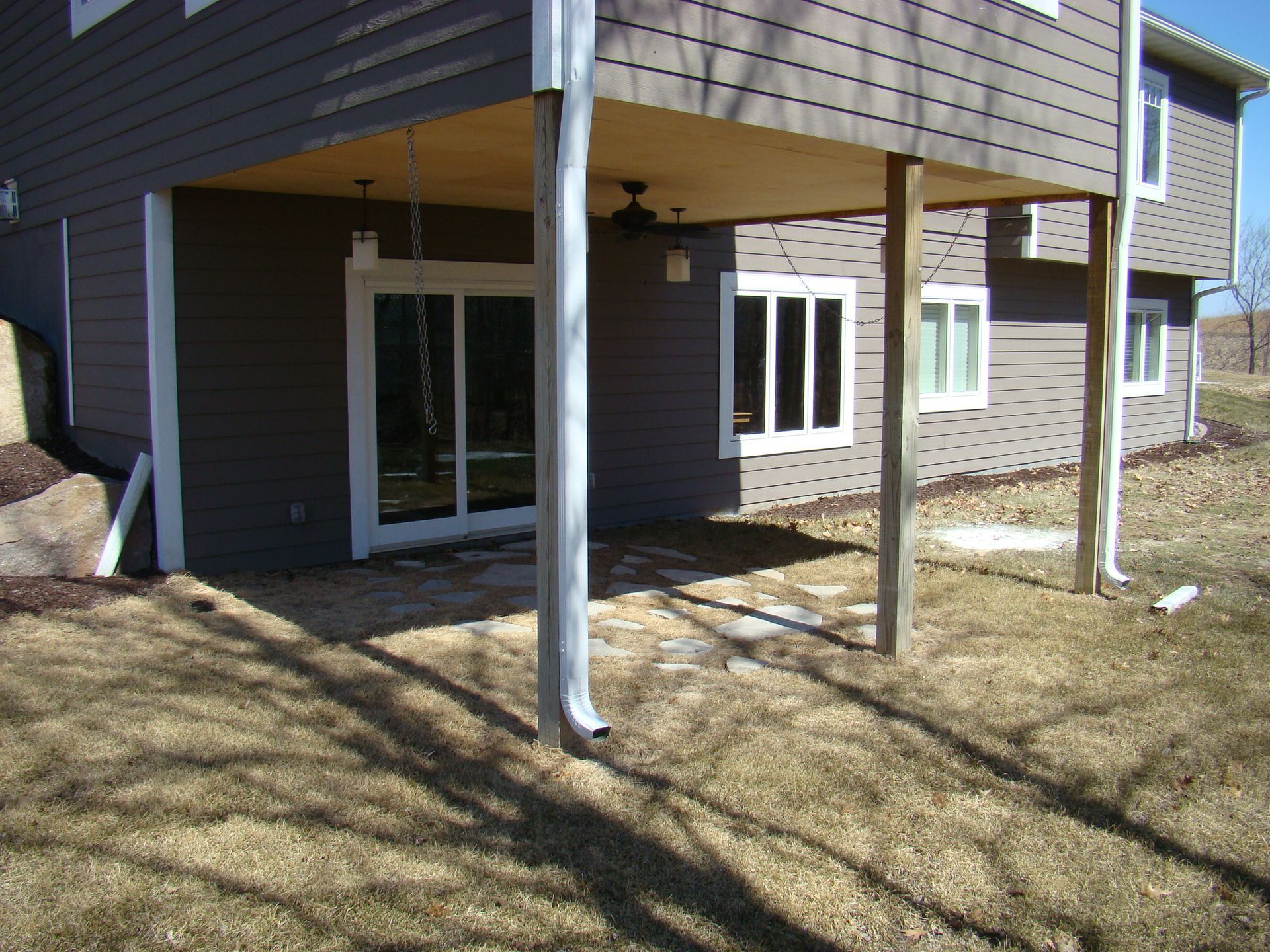 Under deck patio with siding, windows, and downspouts in a grassy yard.