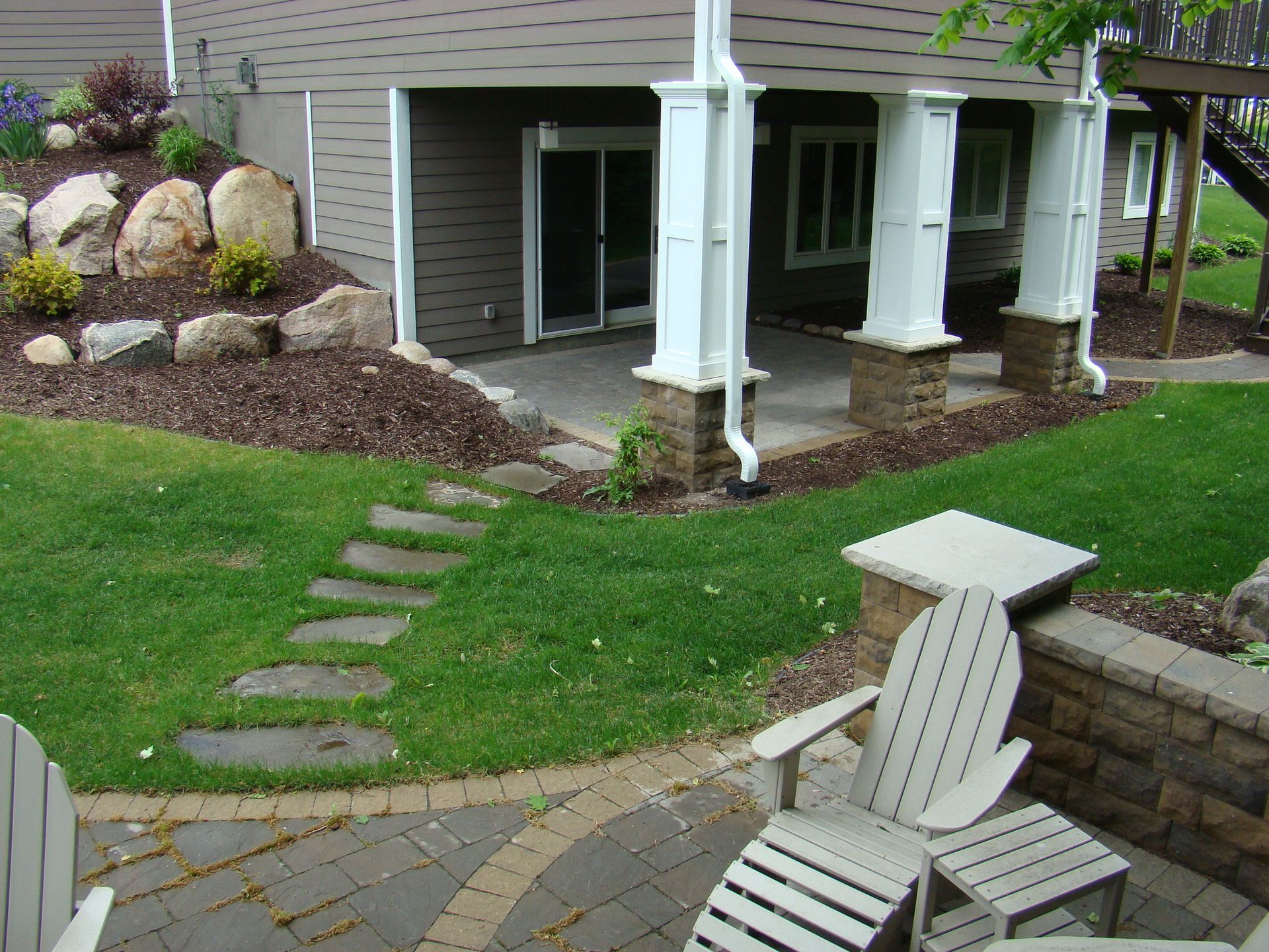Stone pathway leads from a patio to a house with a grass lawn, stone retaining walls, and outdoor seating.