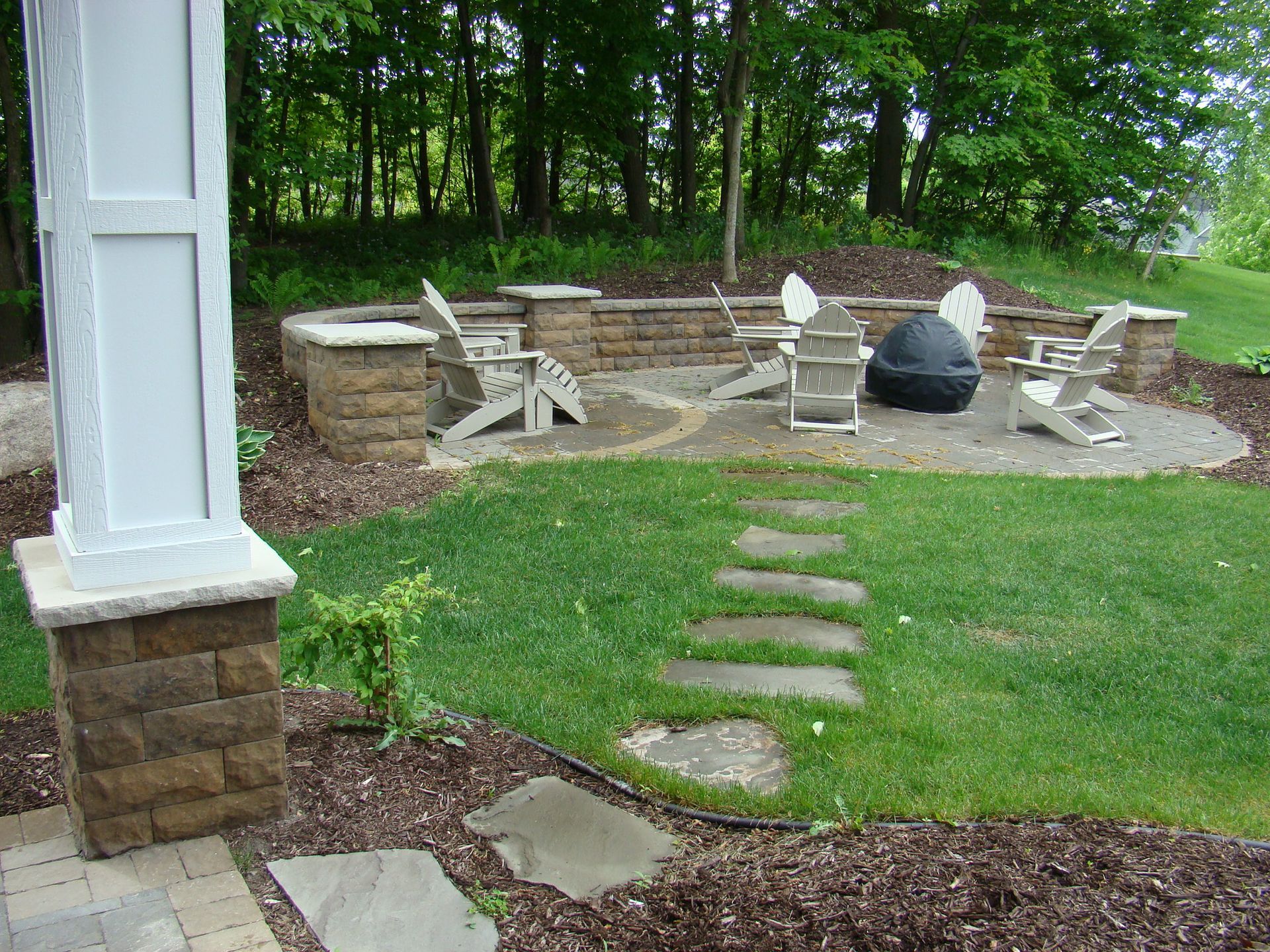 Stone patio with Adirondack chairs, fire pit, and stepping stones in a yard.