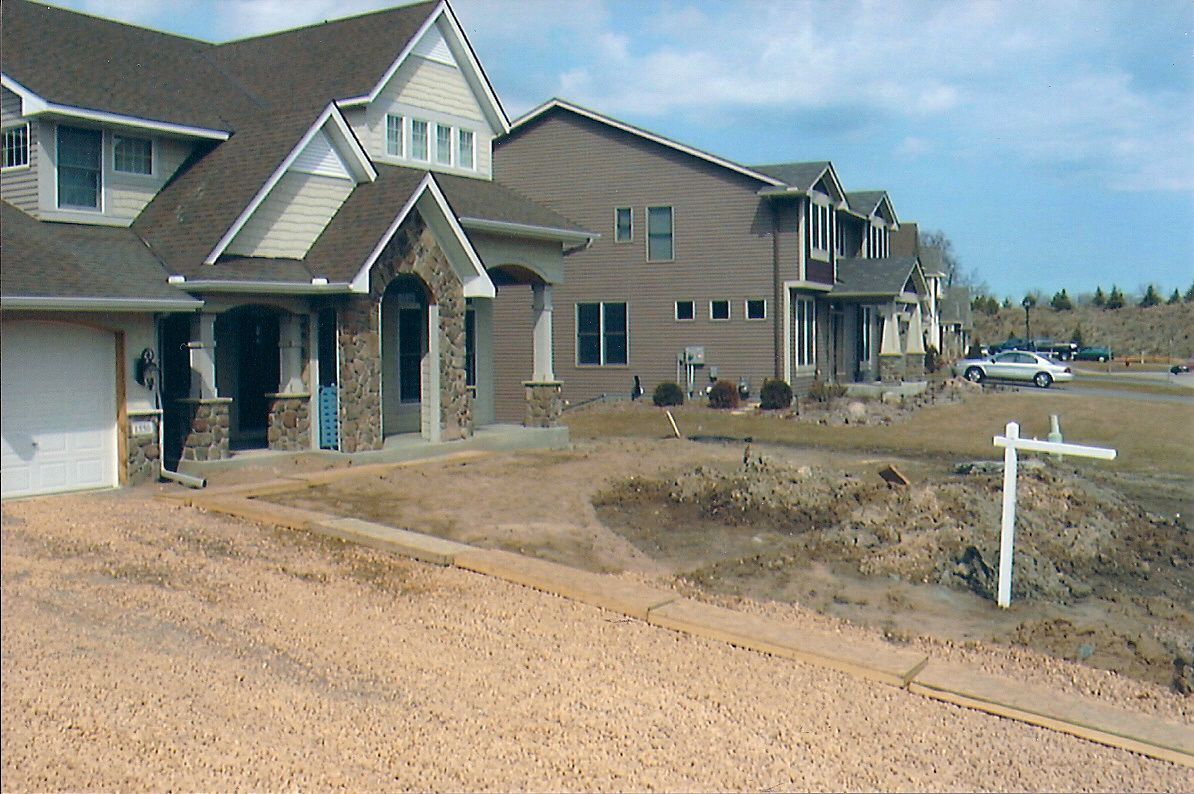 Houses under construction with unfinished driveways and a for sale sign.
