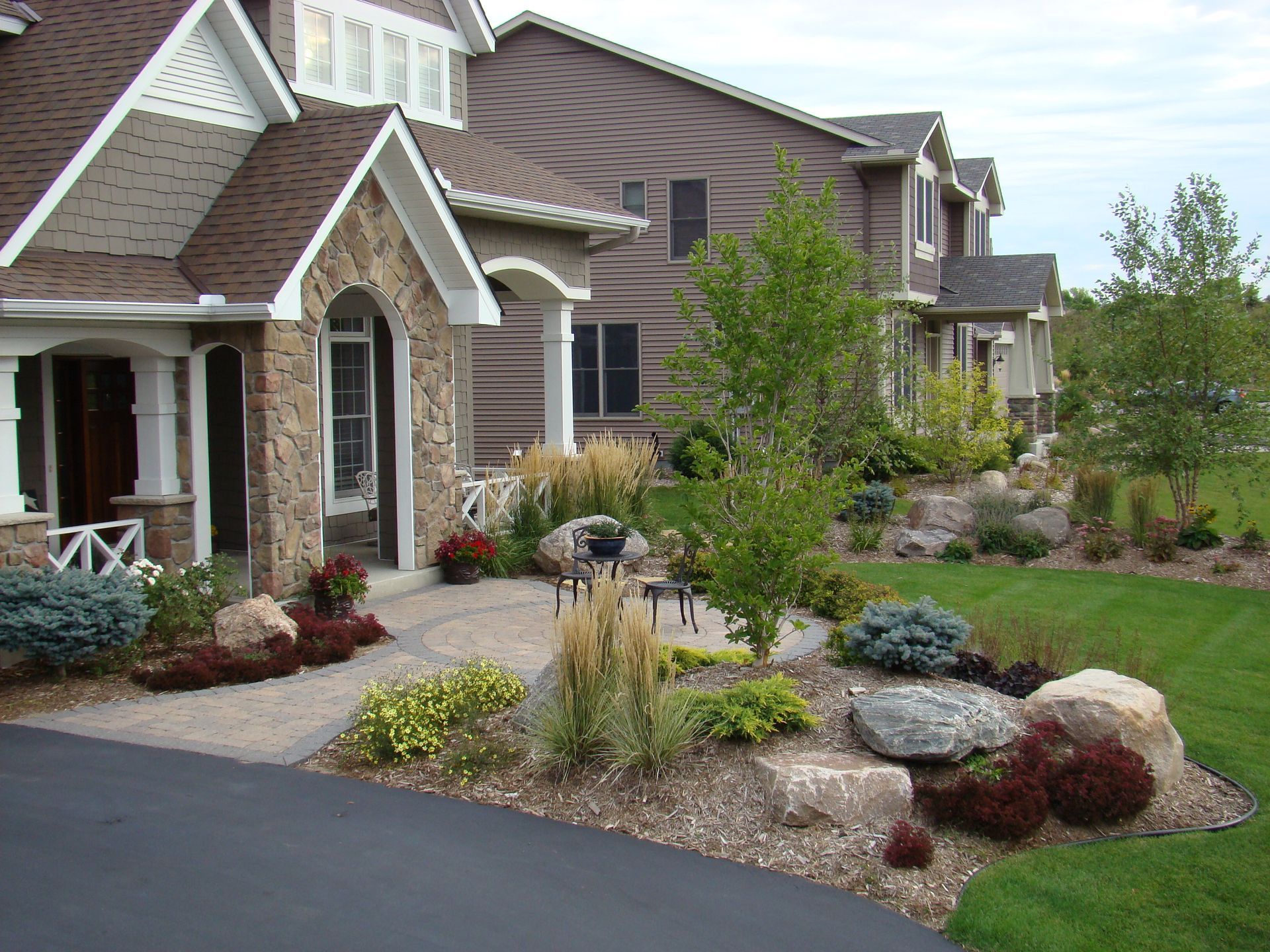Stone-faced house with landscaped yard, pathway, and parked car on a sunny day.