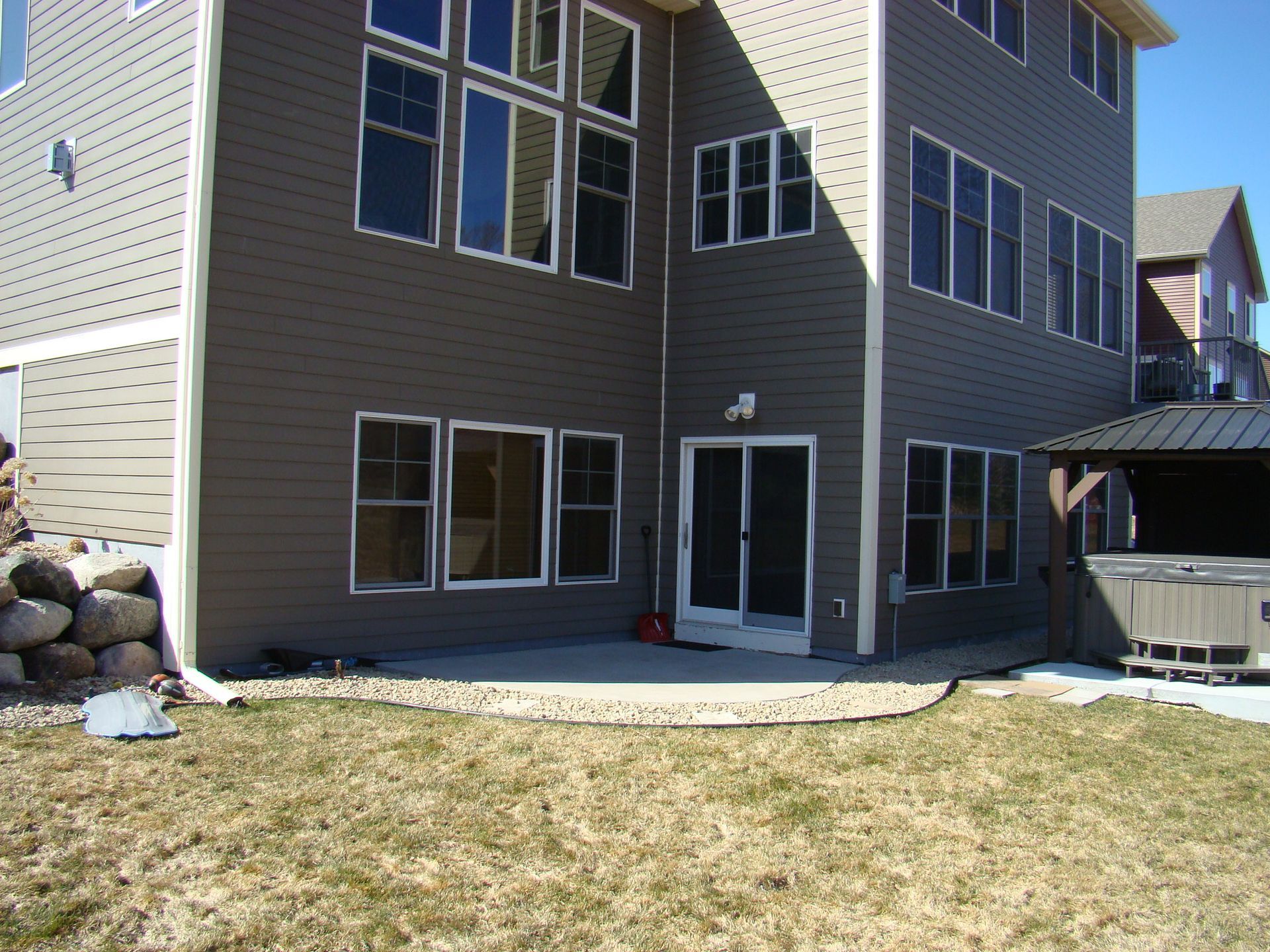 Brown house with many windows and a patio, next to a grassy yard.