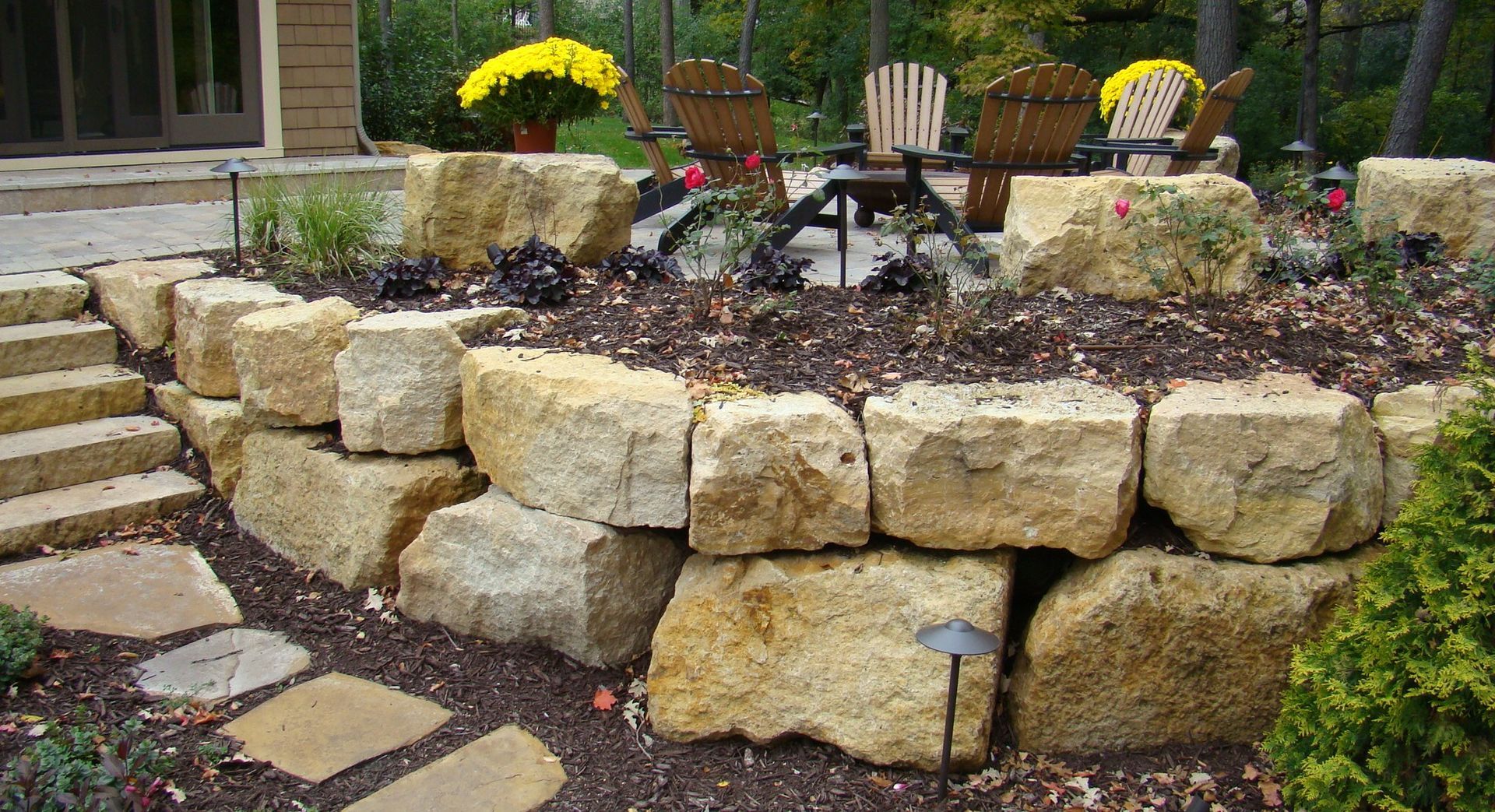 Stone retaining wall with a garden bed and patio furniture in the background.