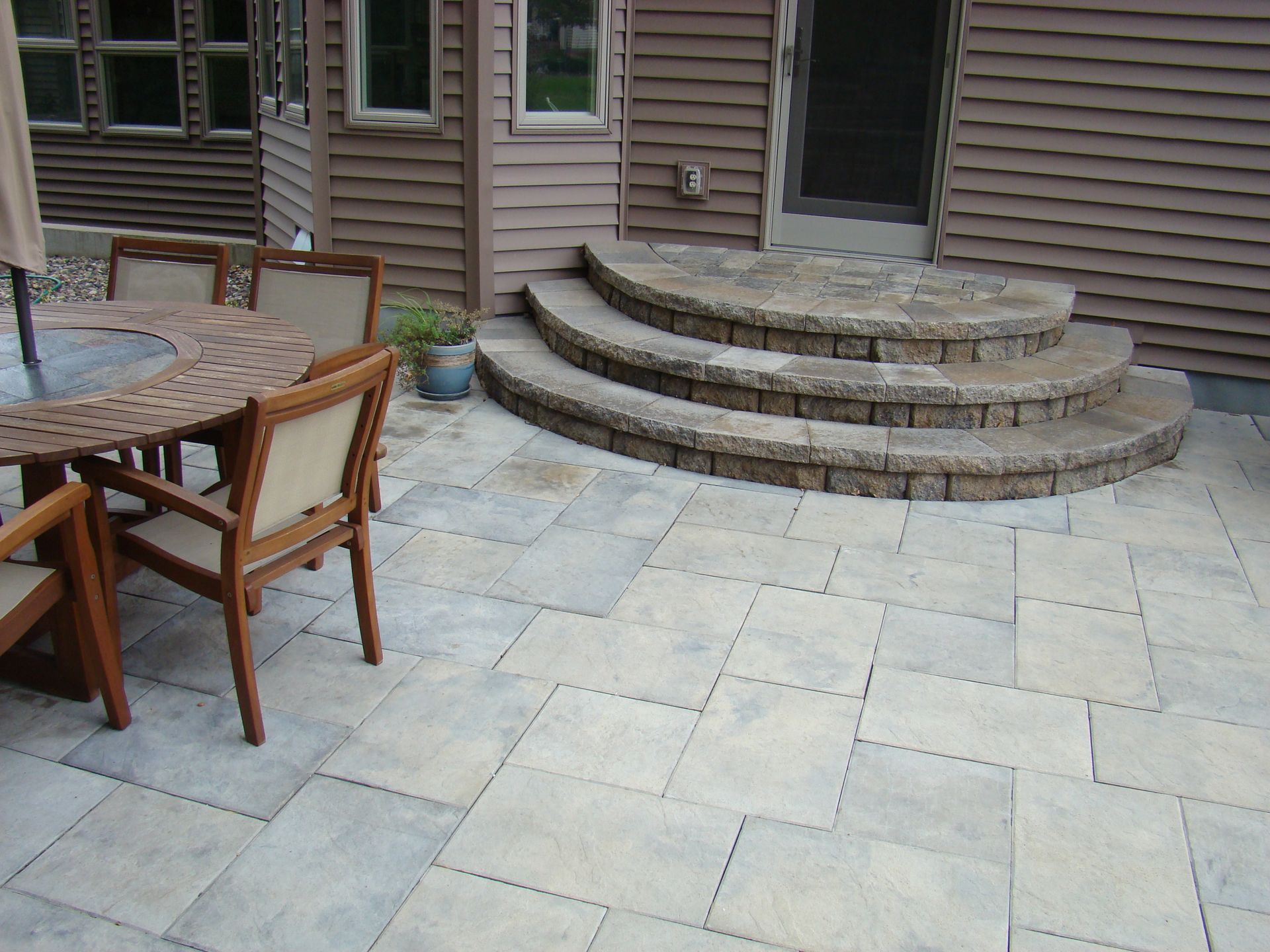 Patio with stone pavers, wooden furniture, and steps leading to a house entrance.