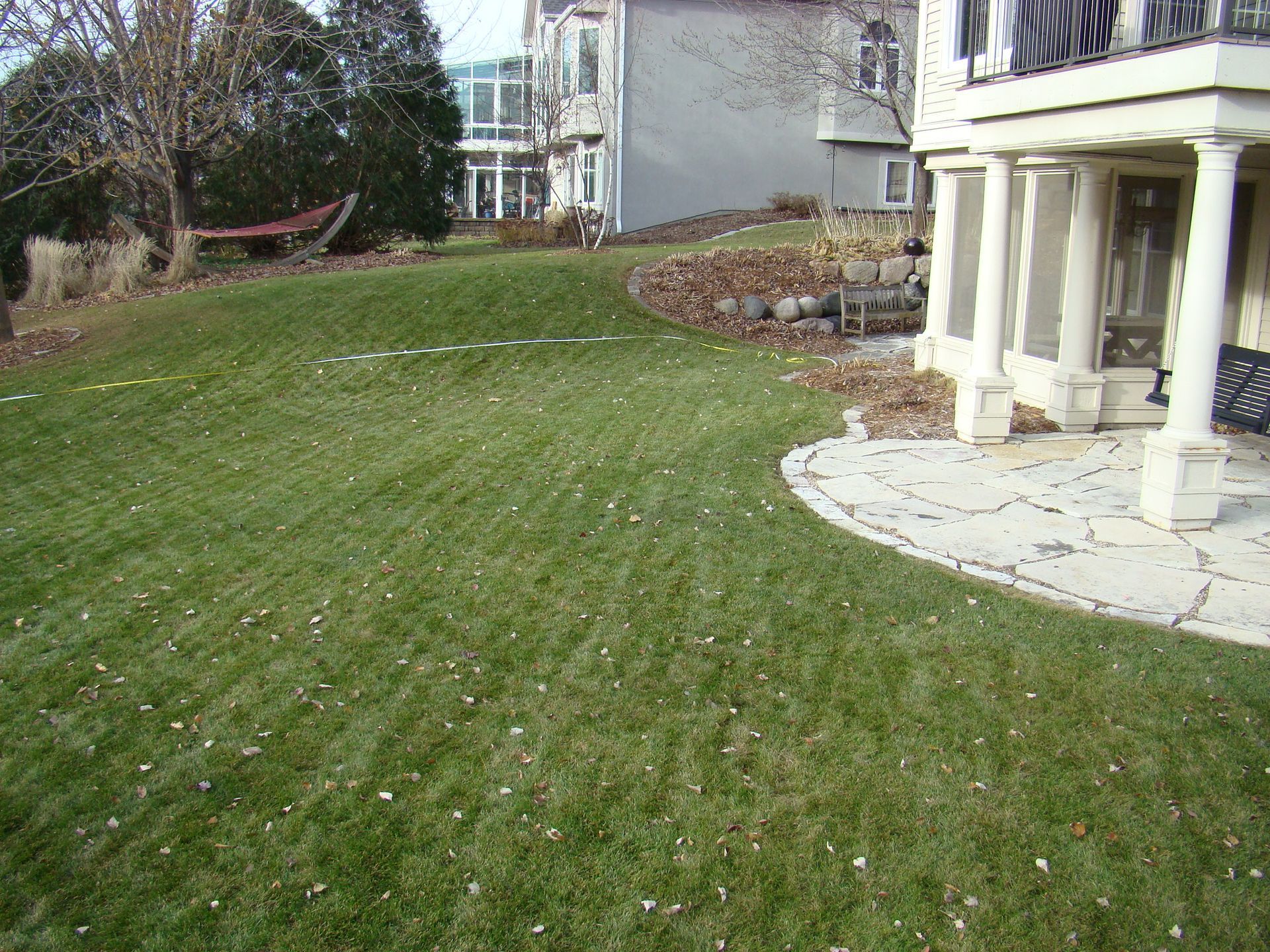 Green lawn sloping towards a house with columns and a flagstone patio.