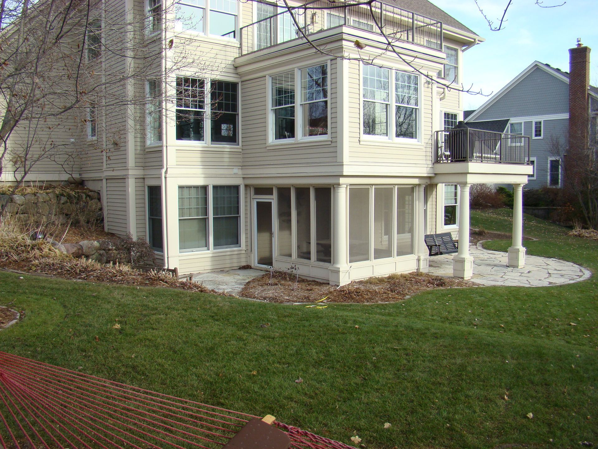 Beige two-story house with a screened porch and deck, set on a green lawn.