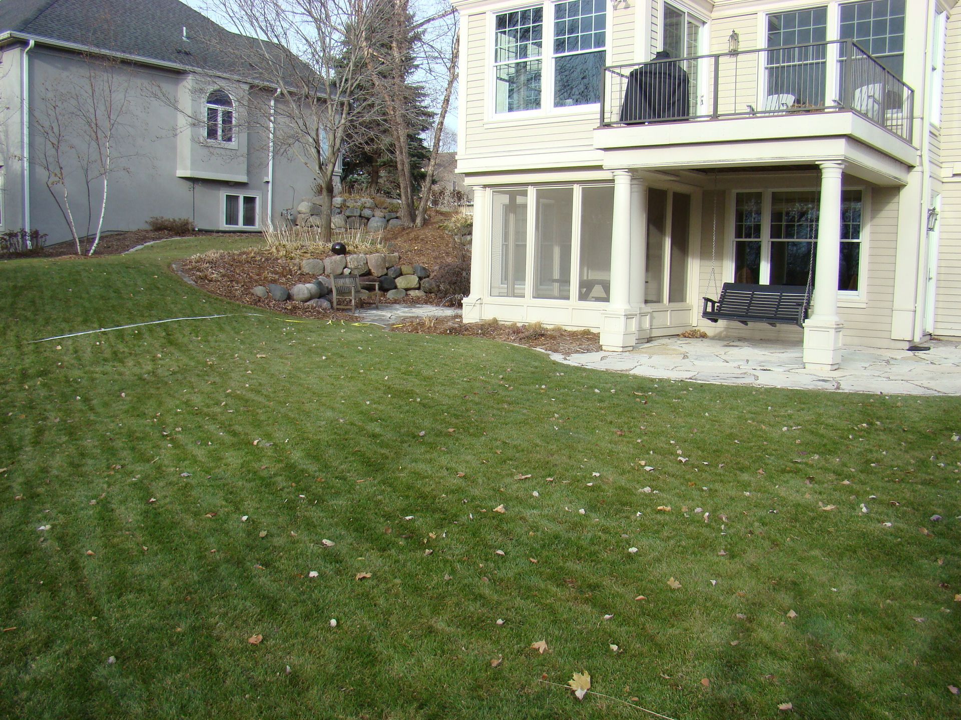 Lawn slopes down toward a house with a screened porch and a balcony. A second house is in the background.