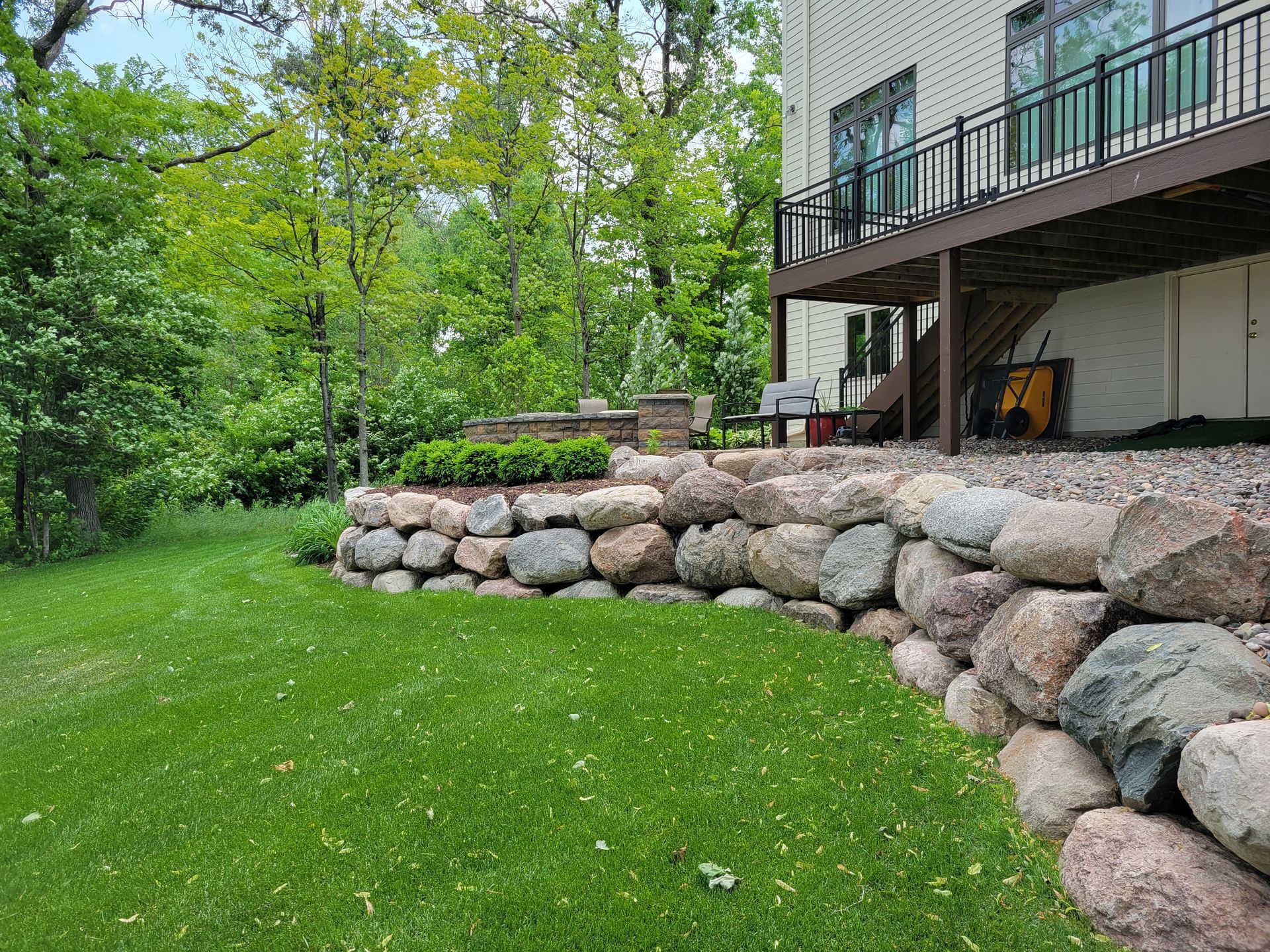A multi-level stone retaining wall in a green yard with a house and trees in the background.
