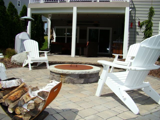 Patio with white Adirondack chairs around a fire pit under a covered deck.