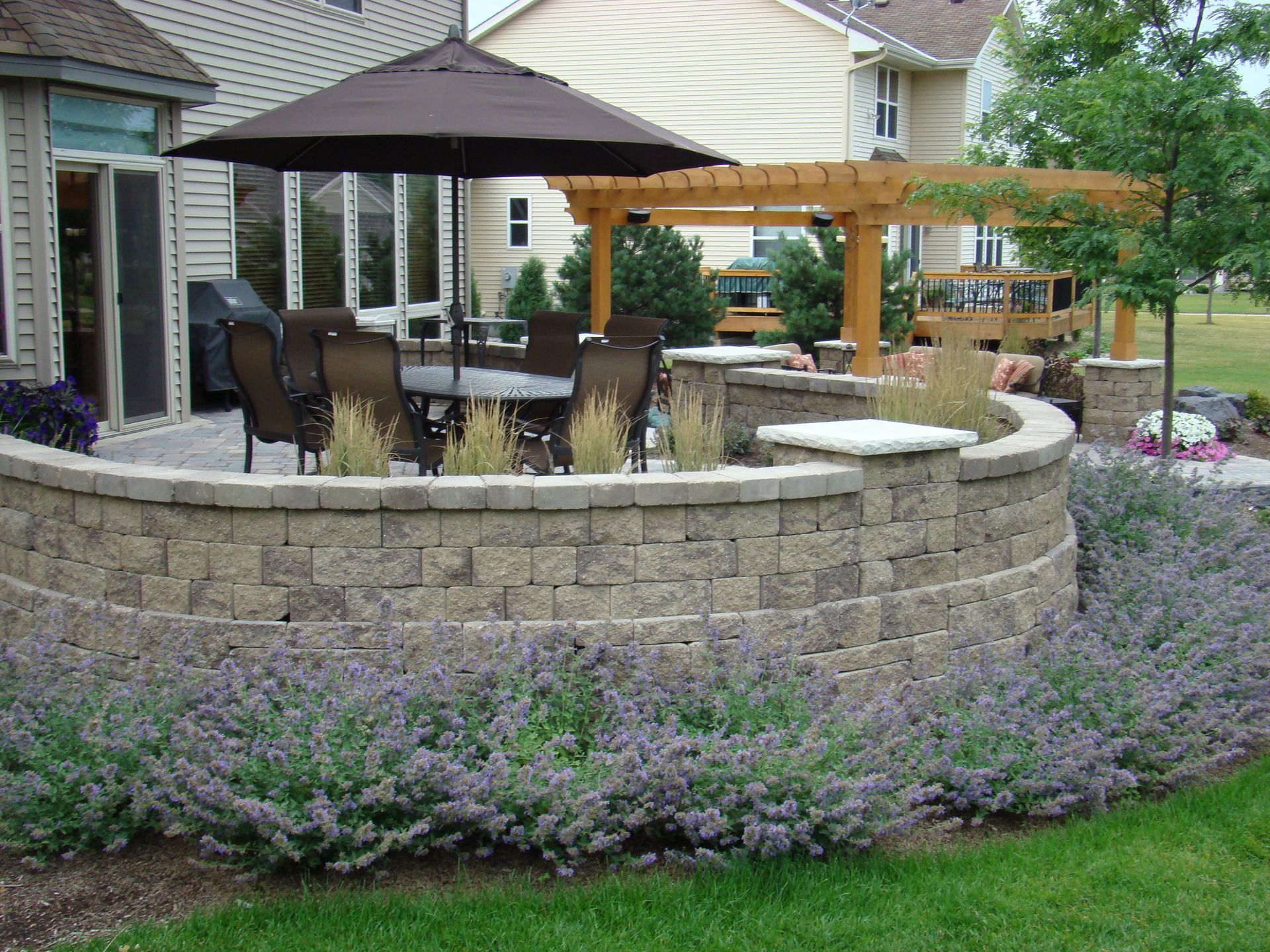 Backyard patio with umbrella, seating, and low retaining wall with lavender bushes.