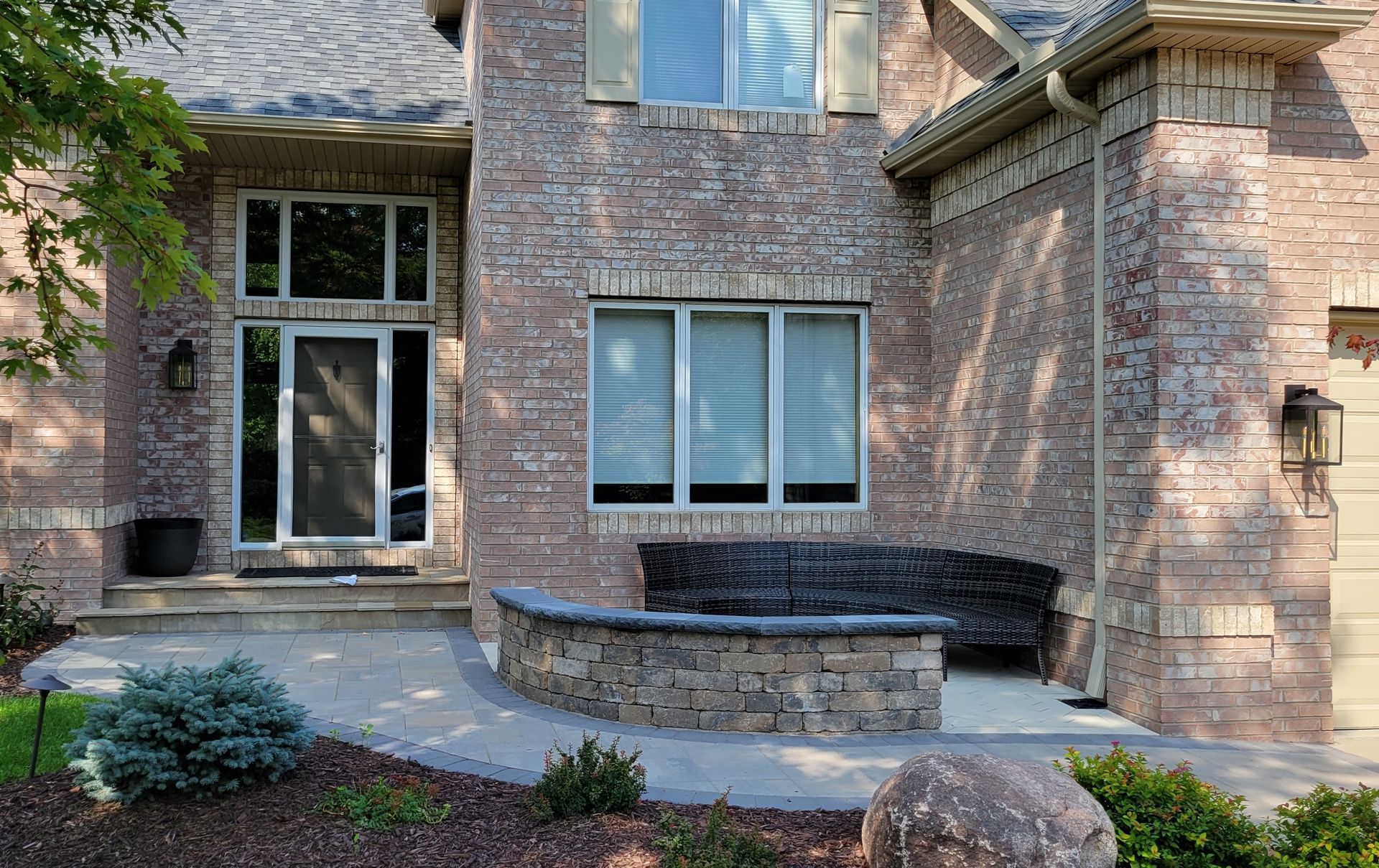 Brick house exterior with a curved stone bench, glass windows, and a doorway.