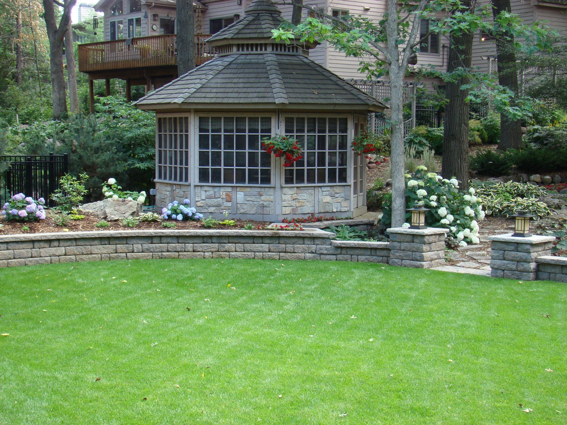 Gazebo with stone base and screen windows in landscaped yard.