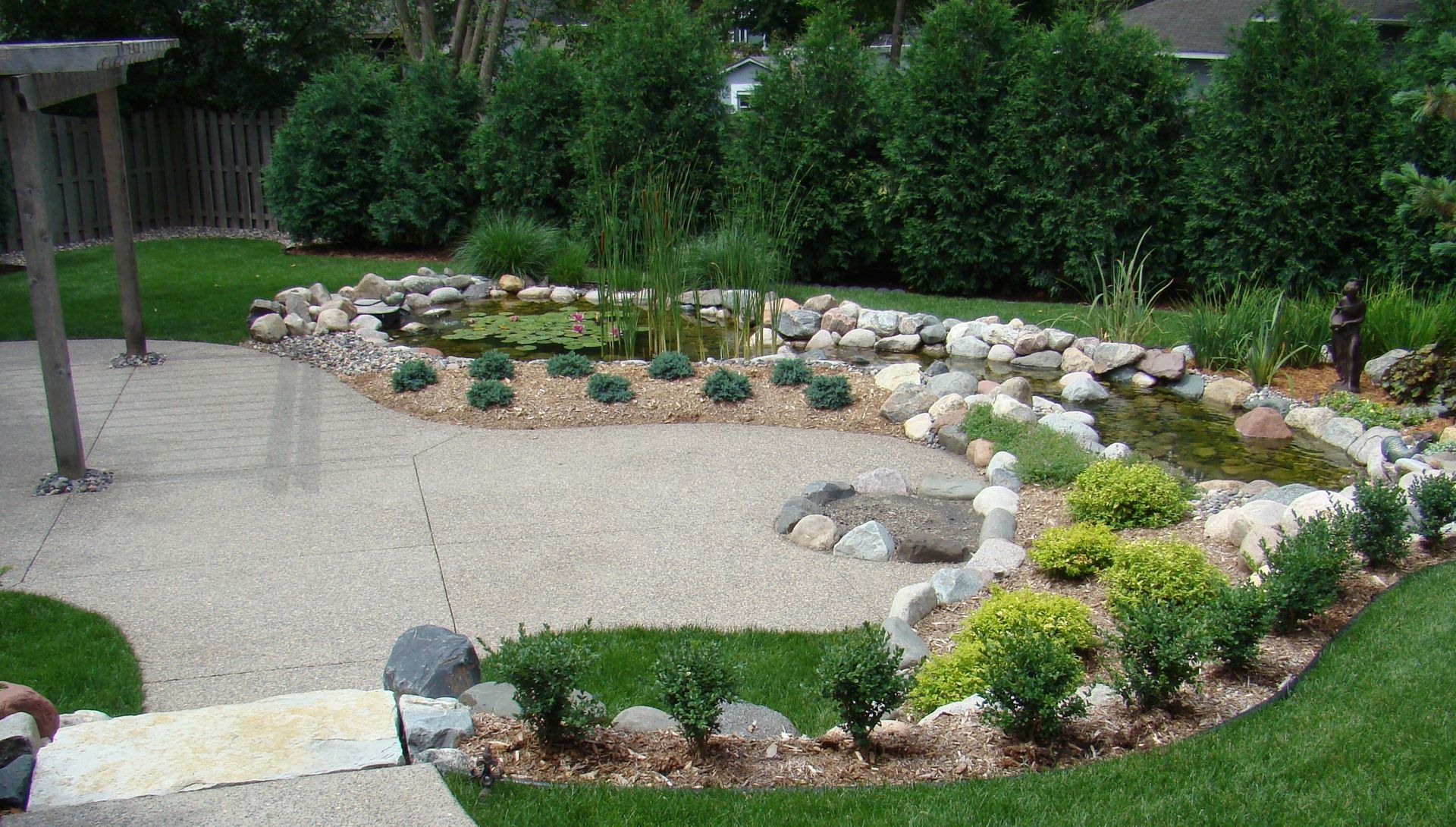Landscaped backyard with pond and stone border, green grass, and patio.