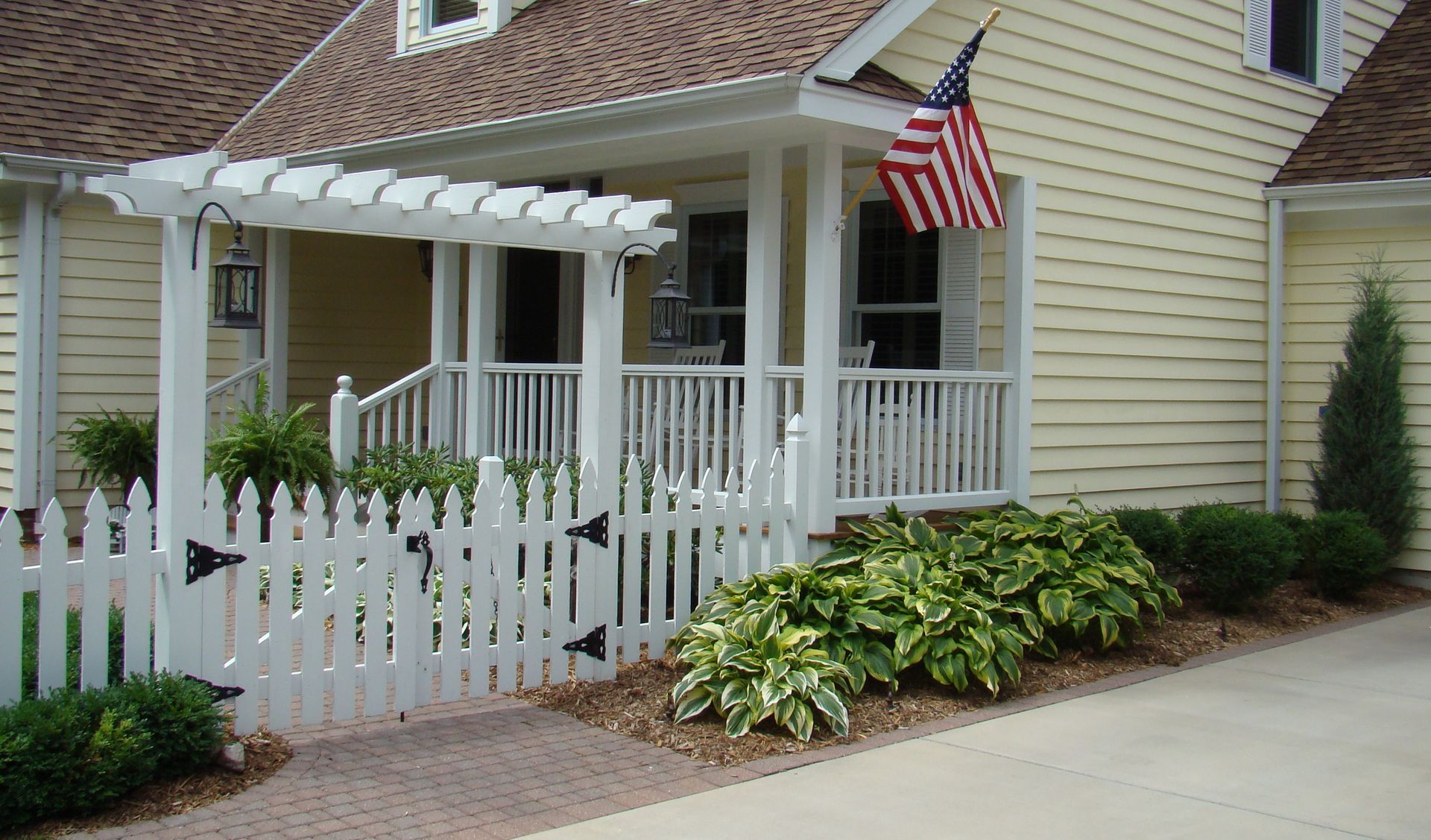White picket fence and porch with an American flag on a yellow house.